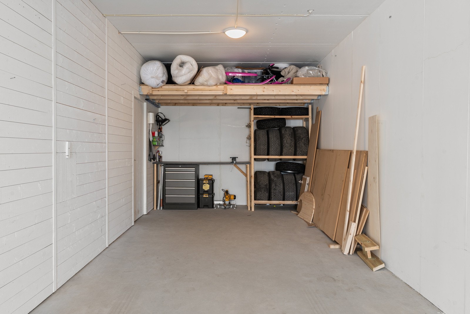 I bakkant av garasje er det etablert oppbevaringshems, arbeidsbenk og hyller for feks bildekk.
