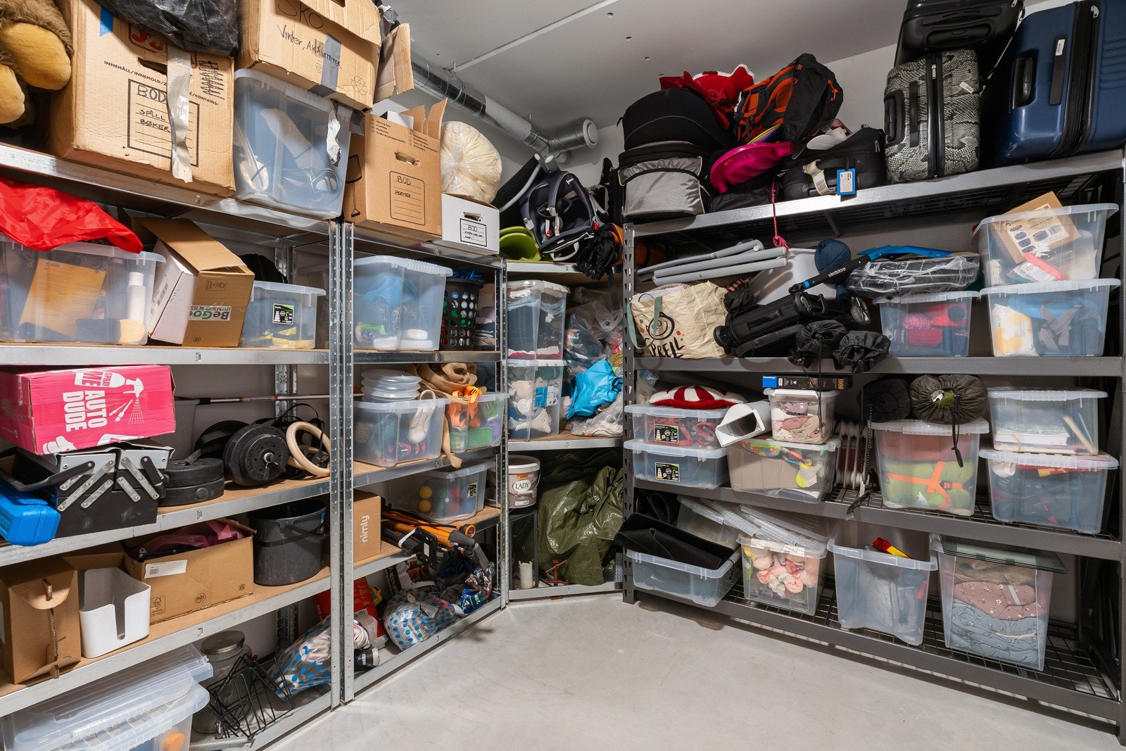 Rikelig med lagringsplass i garasjen, hvor man har en stor sportsbod på ca 12m². Her er det satt inn reoler med plass for oppbevaringsbokser m.m. Svært praktisk! (Hyllereol til høyre medfølger ikke handelen)