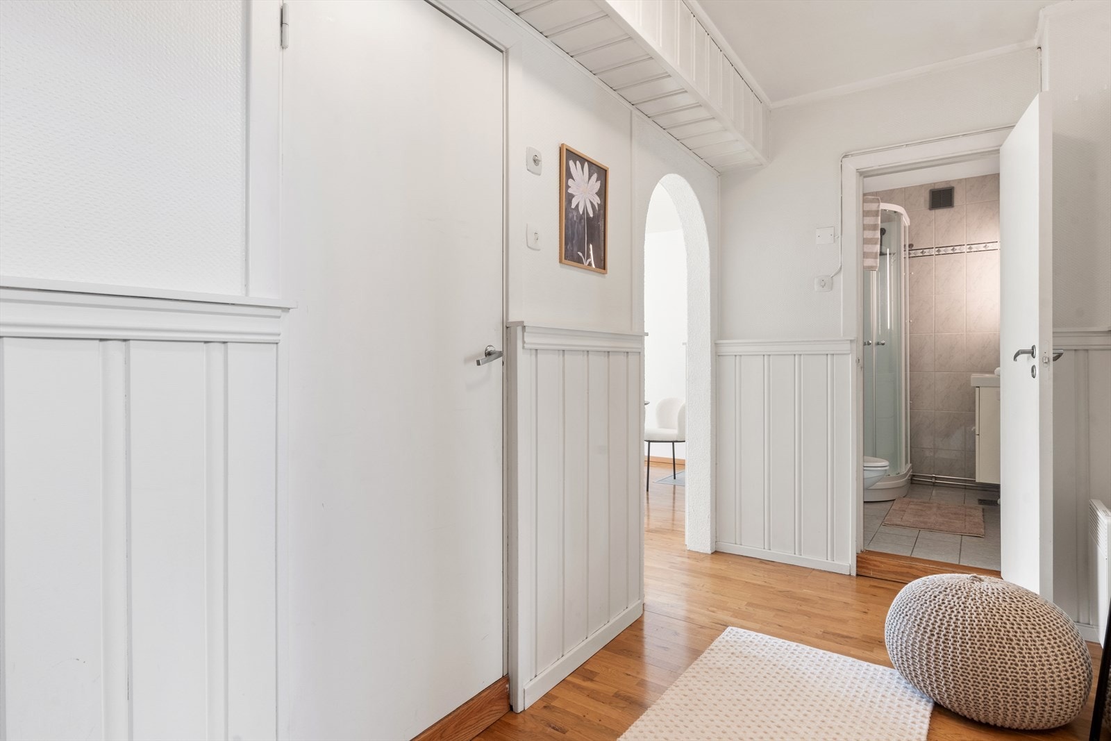 En varm og hyggelig gang med hvit brystpanel og parkett. Dører til vaskerom og bad. Åpen bue til stue. Galleribilde