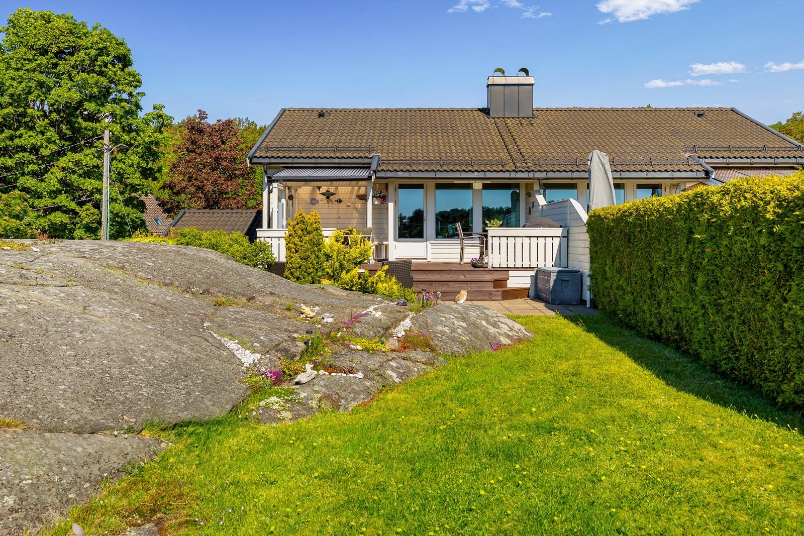 Fra terrassen leder en trapp ned til hagen, hvor uteområdet fortsetter med pent opparbeidet belegningsstein og videre over i grønt plenareal. Galleribilde
