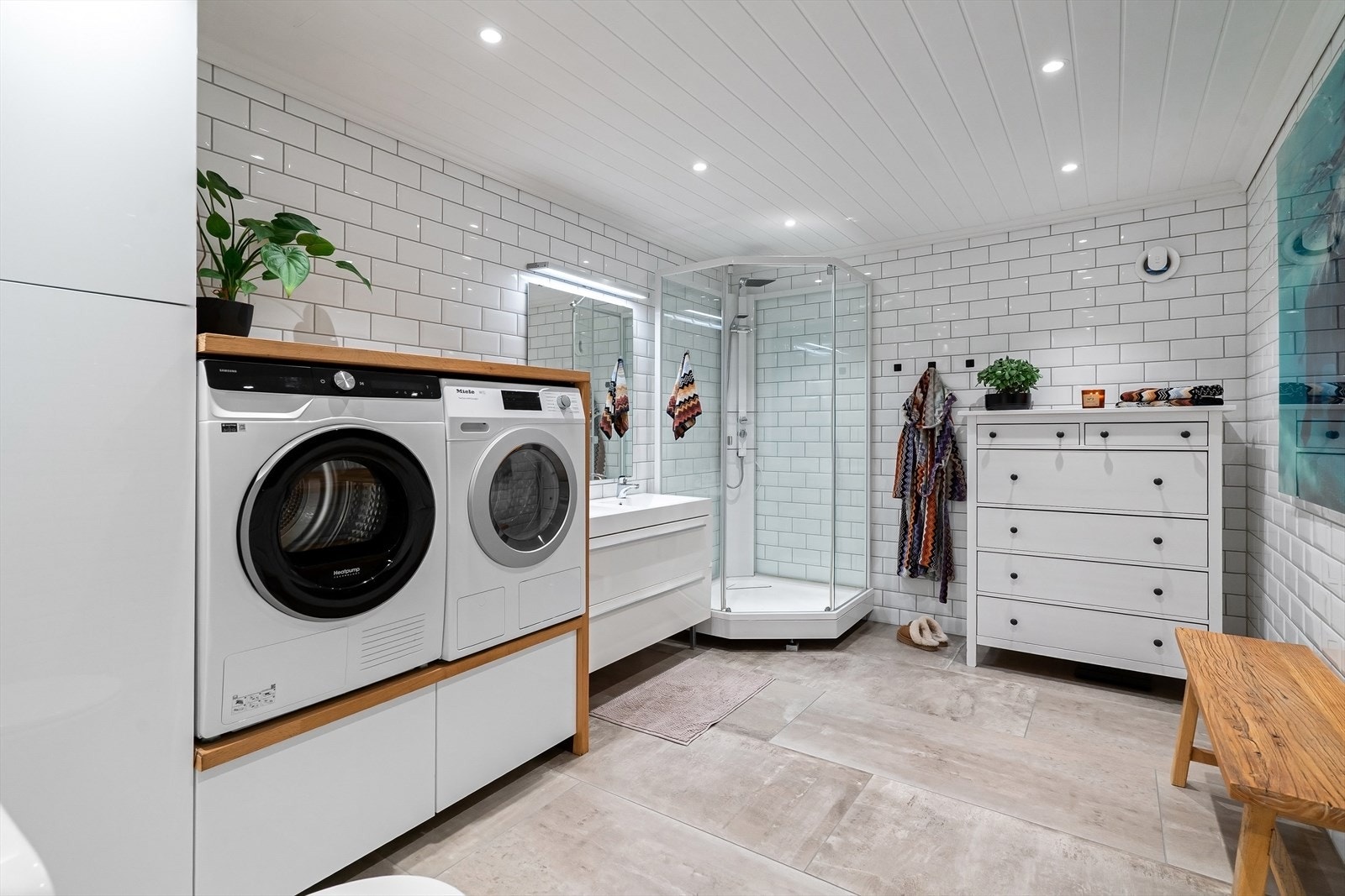 I underetasjen ligger et stort og romslig bad/vaskerom med flislagt gulv med varme, flislagte vegger og panel i taket med downlightsbelysning. Galleribilde