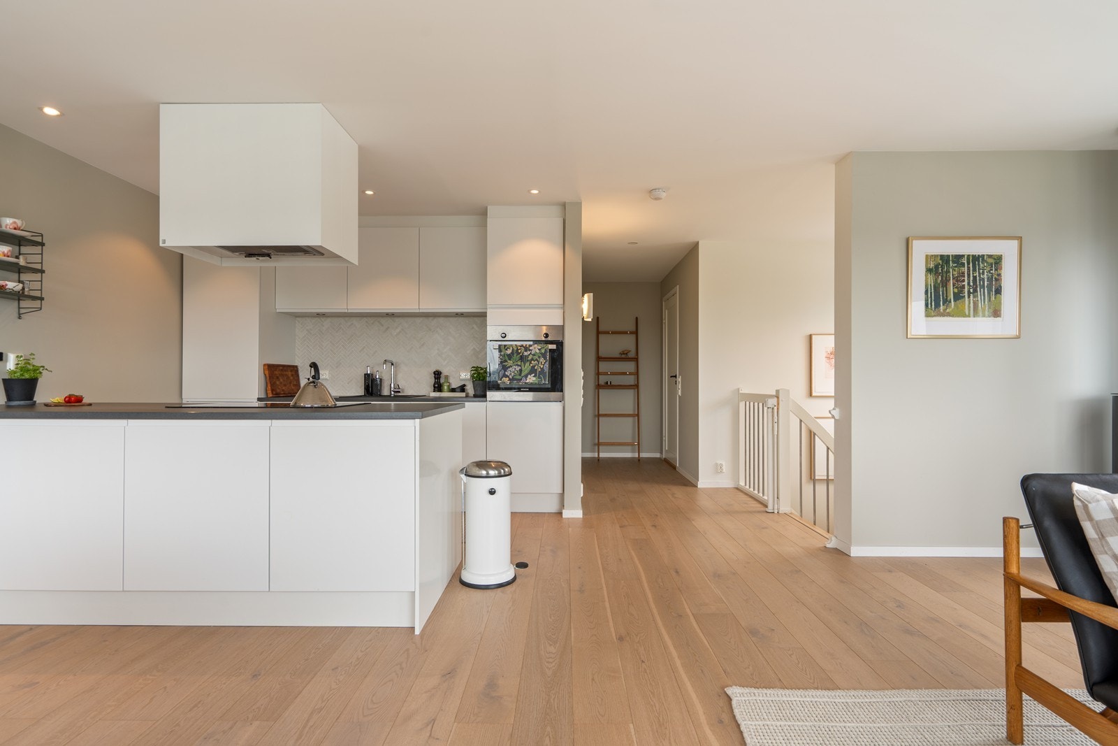 Stilrent og moderne kjøkken bestående av en takhøy innredning, utført med hvite, slette fronter og benkeplate av laminat med nedfelt vask. Galleribilde