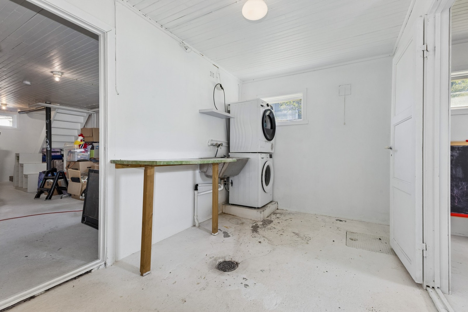 Praktisk vaskerom i kjelleren med opplegg for vaskemaskin, utslagsvask i rustfritt stål og sluk i gulvet. Galleribilde