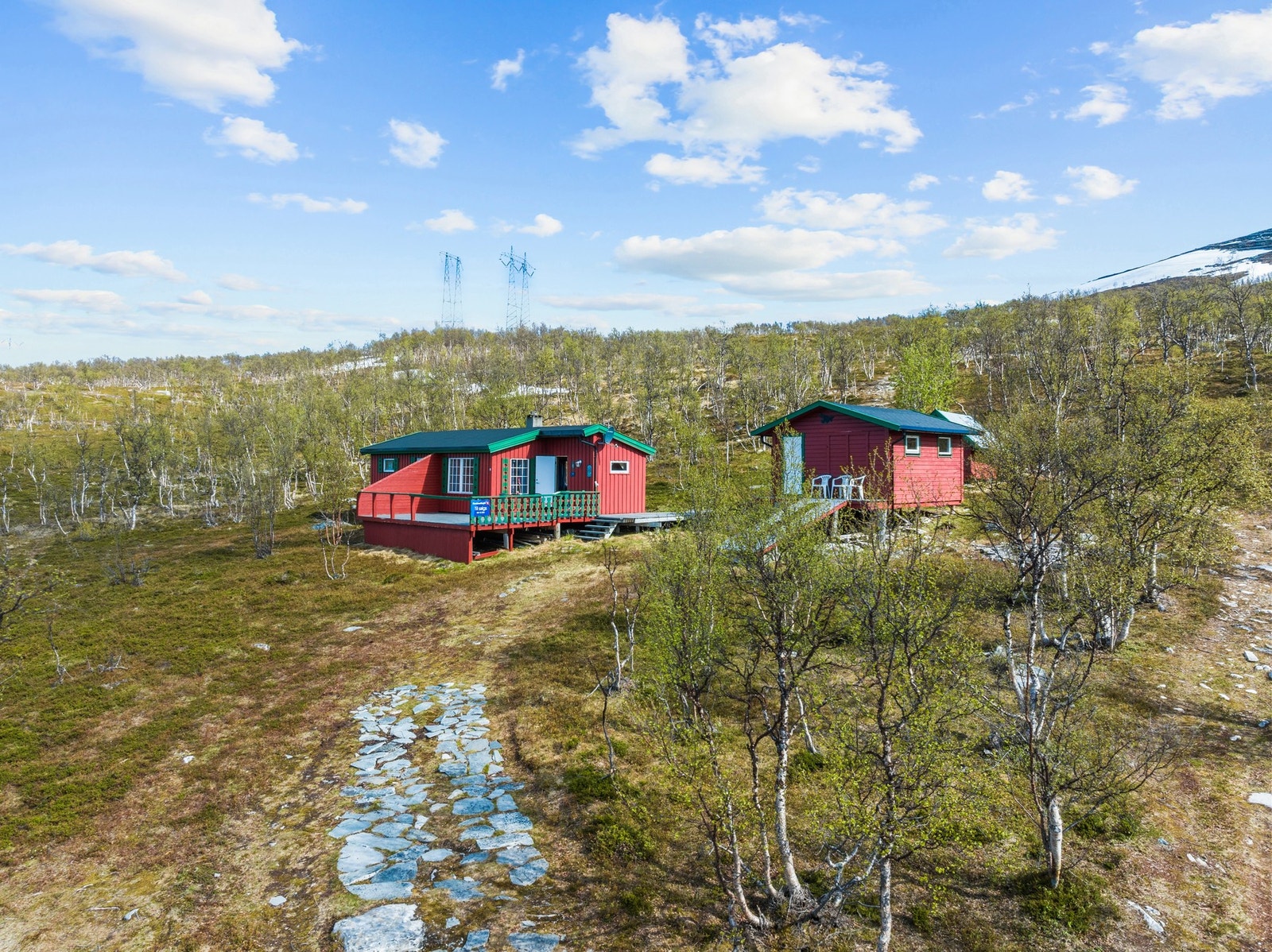 Fasaden har stående bordkledning, og hytta er fundamentert på trepåler. Galleribilde
