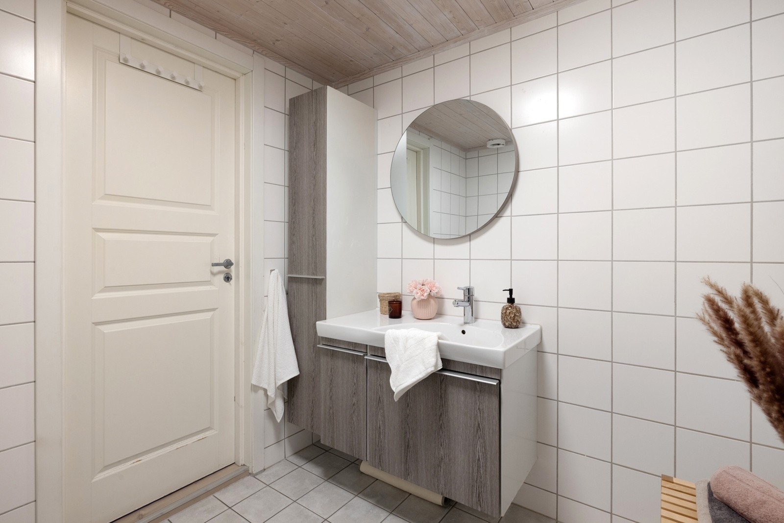 Badet er flislagt og innredet med dusjhjørne med innfellbare glassdører, vegghengt toalett samt en baderomsinnredning med heldekkende servantplate. Galleribilde