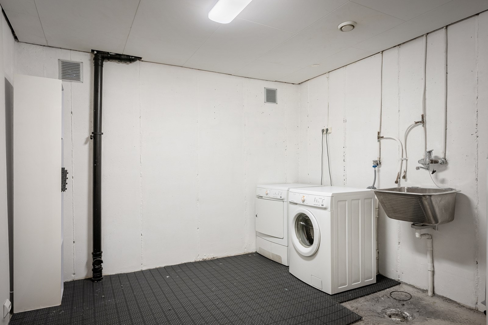 Romslig vaskerom med betonggulv, sluk, utslagsvask og opplegg for vaskemaskin. Galleribilde