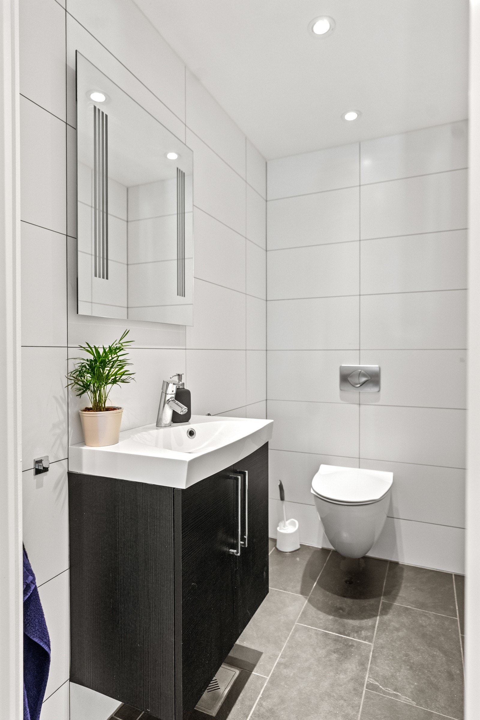 Gjeste-wc med flislagte overflater og vegghengt toalett. Innredningen består av servantskap med heldekkende servant. Over servanten er det montert speil med integrert belysning. Ventilasjon er mekanisk. Galleribilde