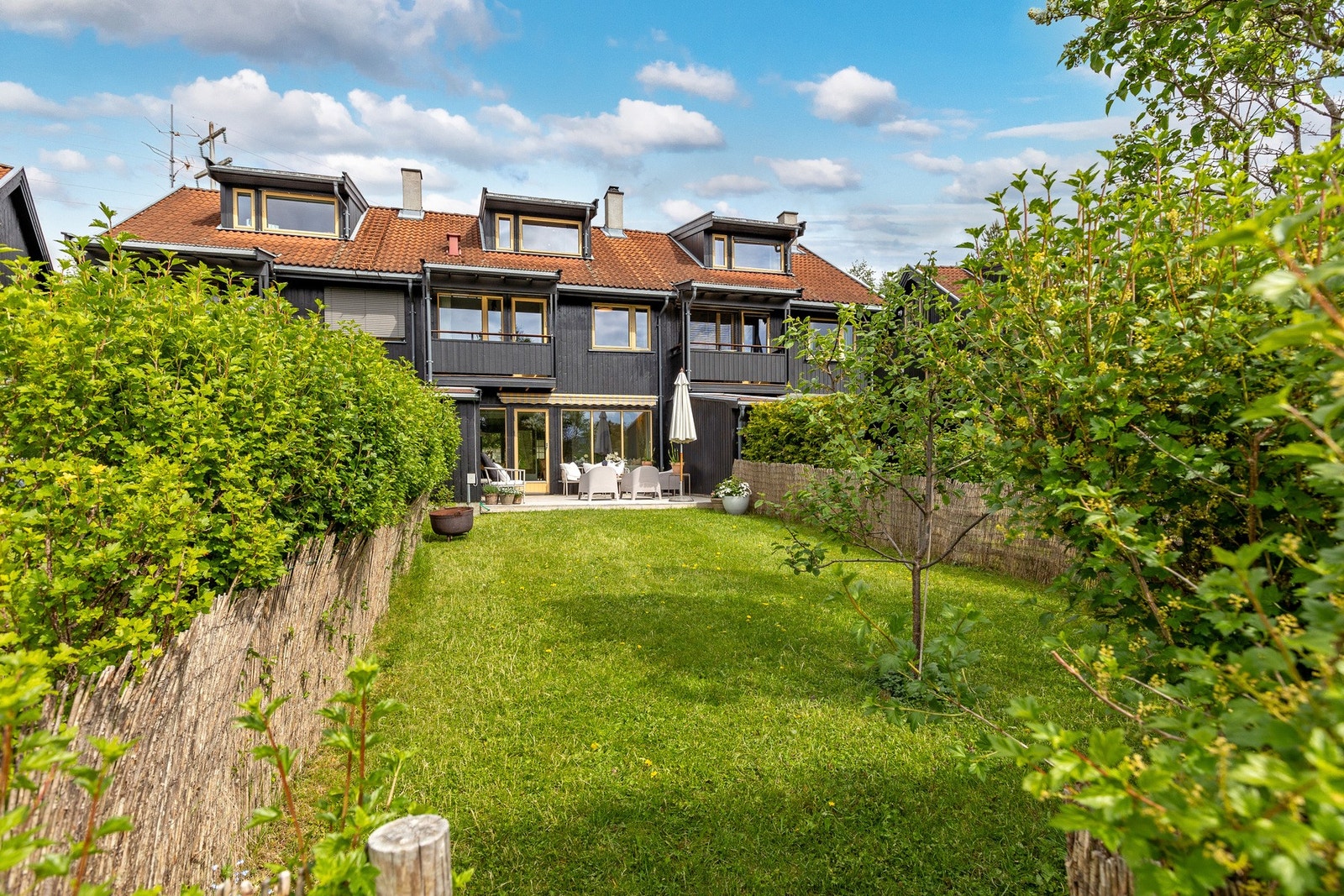 Boligen sett fra hagesiden med terrasse, grøntarealer og en skjermet beliggenhet som gir gode uteopphold gjennom sesongen. Galleribilde
