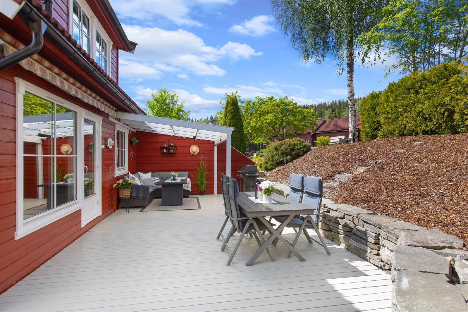 Overbygget gir en lun sone som kan brukes store deler av året, mens den åpne delen slipper inn rikelig med ettermiddagssol, perfekt for avslapning etter jobb eller lange sommermåltider. Over det store stuevinduet er det en stor markise. Galleribilde
