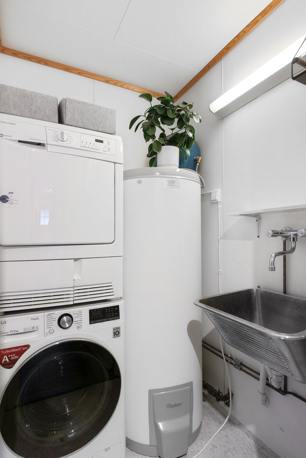 Praktisk vaskerom med opplegg for vaskemaskin og skyllekar ligger vegg i vegg med badet. Galleribilde