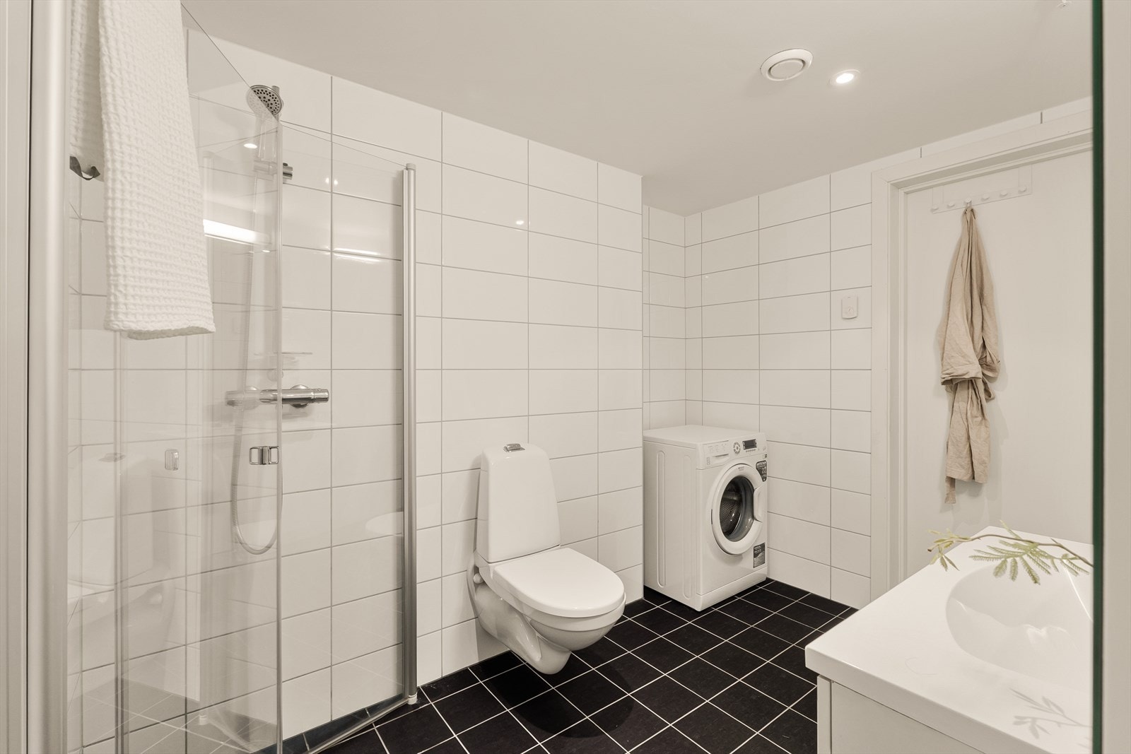 Baderomsinnredning og høyskap i hvit utførelse med slette fronter. Baderommet har opplegg for både vaskemaskin og tørketrommel. Galleribilde