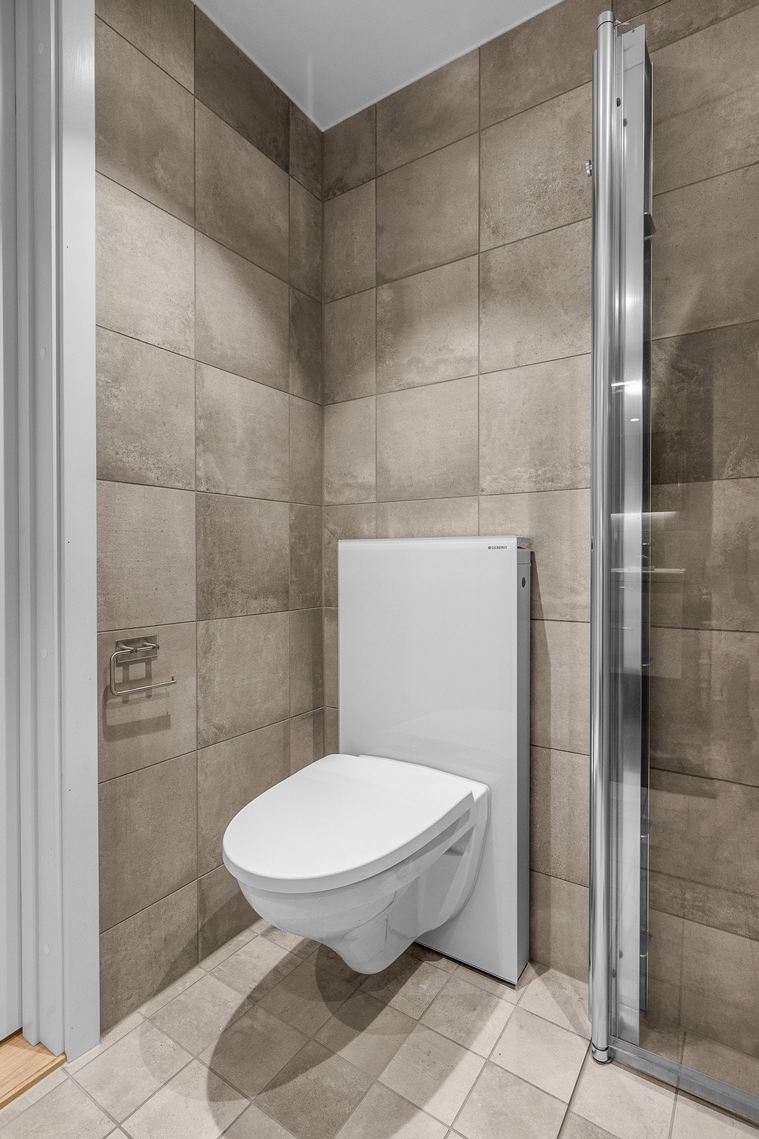Badet er utstyrt med vegghengt toalett og dusjhjørne med innfellbare glassdører. Galleribilde