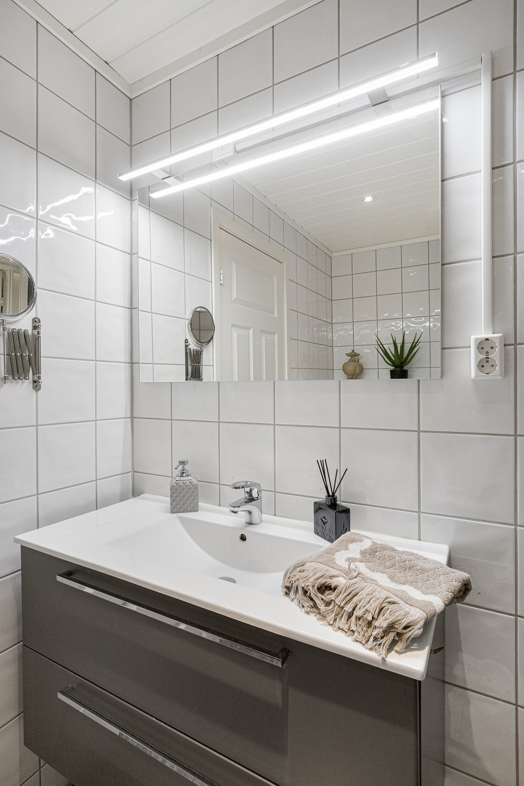 Baderomsinnredningen har grå fronter og består av en heldekkende servant på en skuffseksjon, et høyskap og et stort speil med belysning. Galleribilde