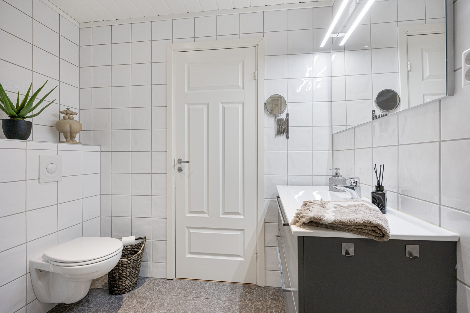 Badet har hvite fliser på veggene, downlights i himlingen og grå fliser på gulv med gulvvarme. Galleribilde