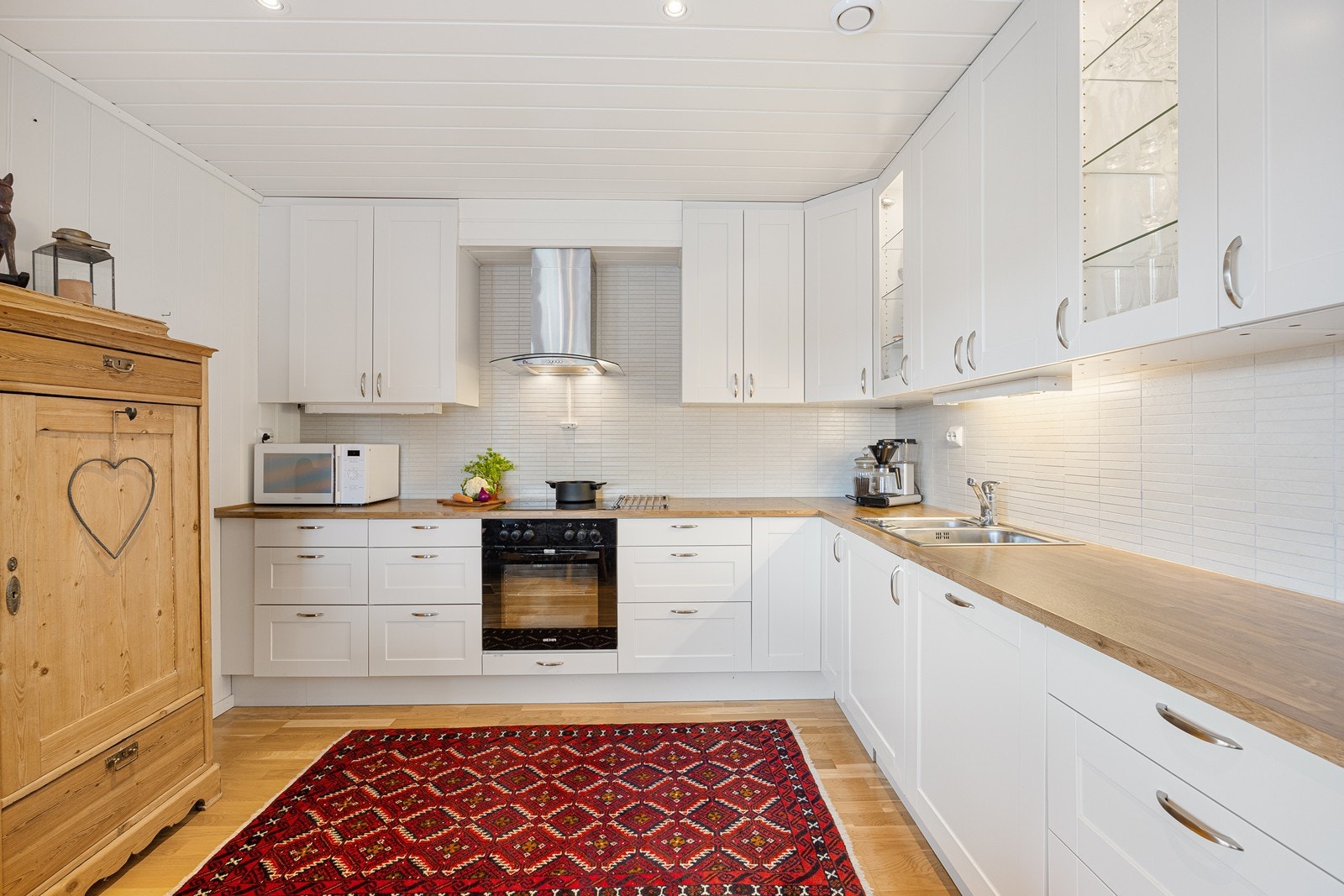 Kjøkkenet har et stilfullt og moderne design med gode benkeflater og rikelig med oppbevaringsplass. Innredningen har hvite, profilerte fronter, vitrinedører, takhøye skap og gyllen laminatbenkeplate med nedfelt kum i stål. Galleribilde