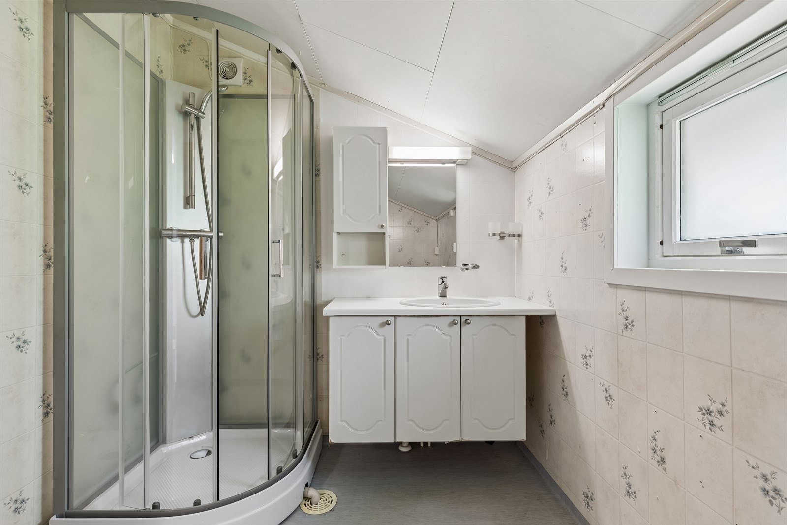 Badet er utstyrt med dusjkabinett og servantinnredning. På gulvet er det vinylbelegg. Galleribilde