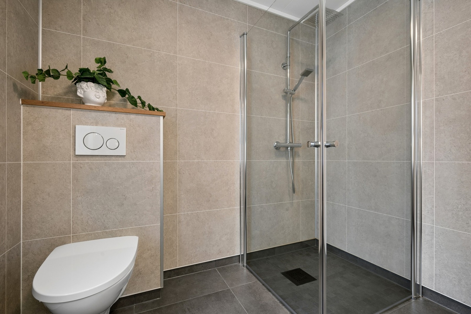 Badet er utstyrt med vegghengt toalett og et romslig dusjhjørne med innfellbare glassdører. Galleribilde