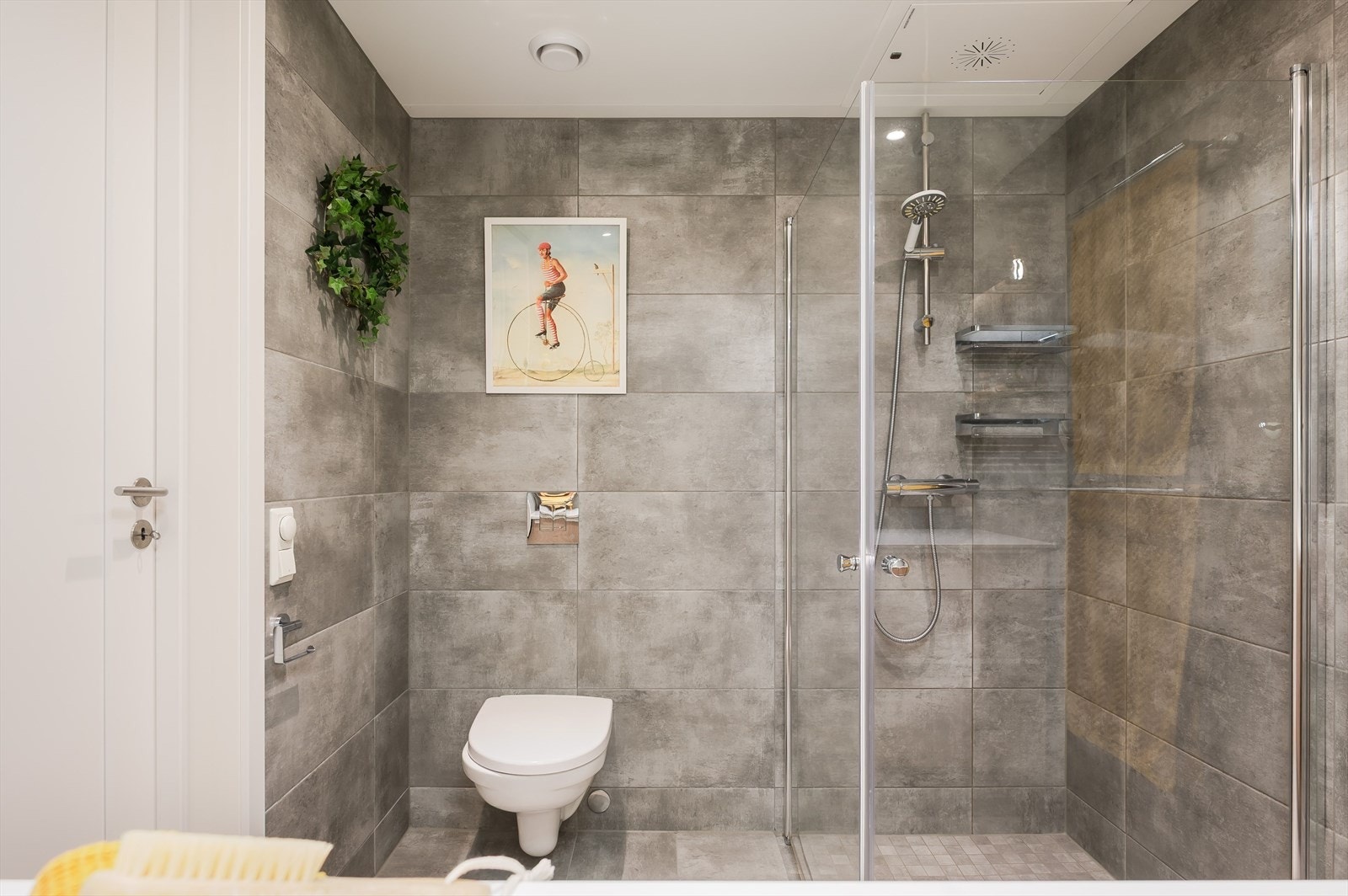 Badet består for øvrig av veggmontert toalett og dusjhjørne med innfellbare dusjdører og veggmontert dusjbatteri. Galleribilde
