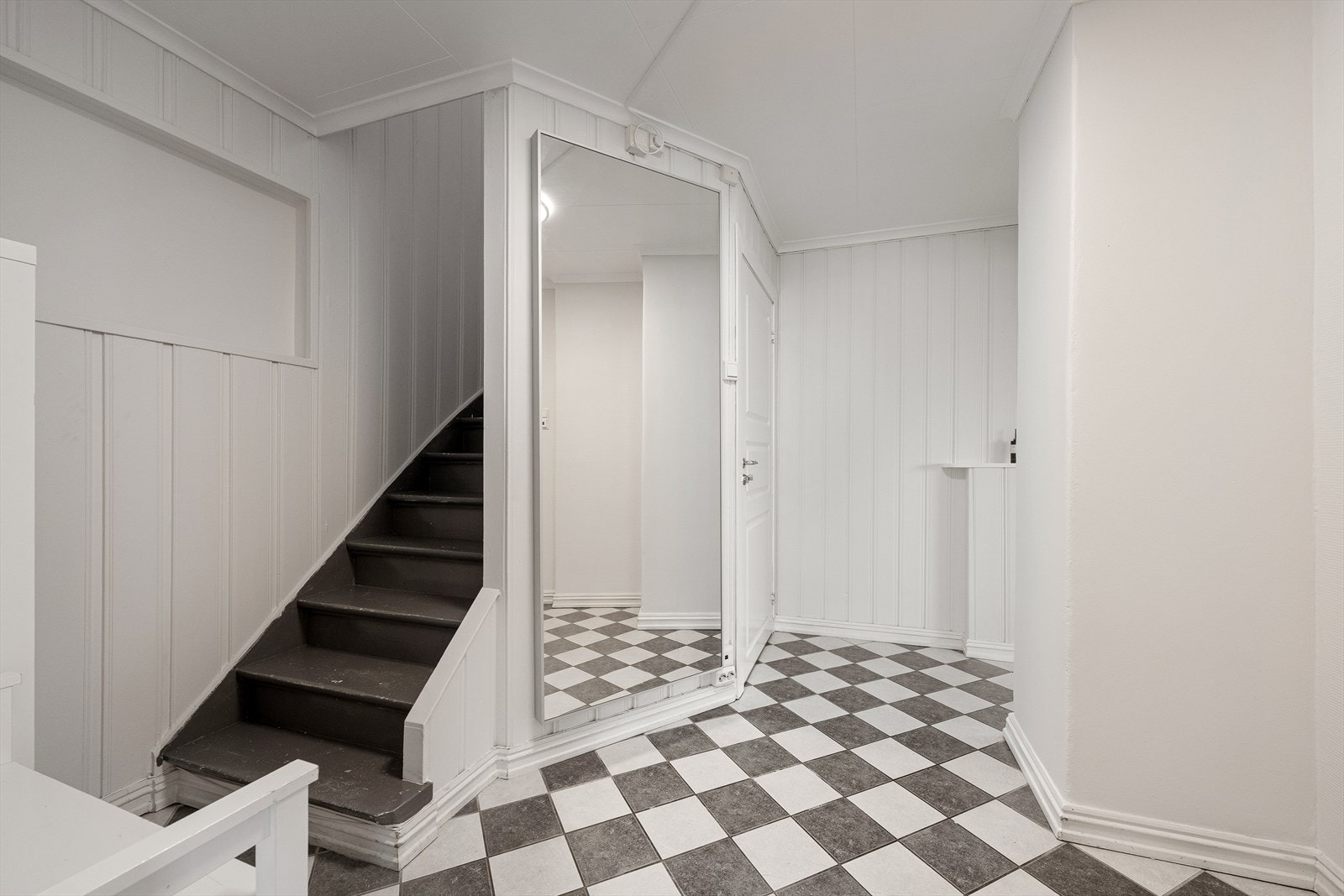 Entréen leder til en malt tretrapp opp til leilighetens loftsetasje. Galleribilde