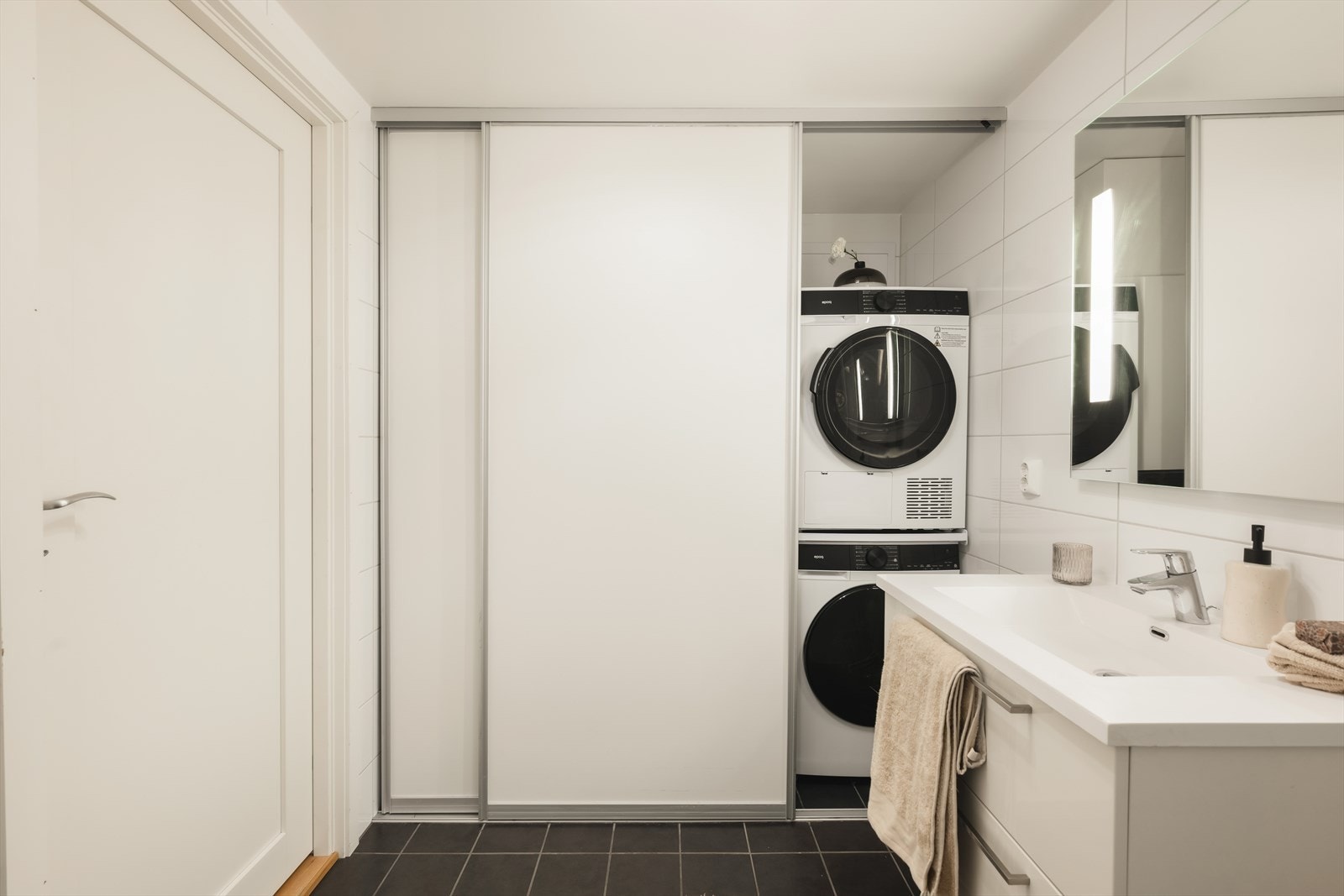 En smart skyvedørsløsning skjuler vaskesonen med opplegg for vaskemaskin og plass til tørketrommel samt oppbevaring, noe som gir et ryddig og helhetlig uttrykk. Galleribilde