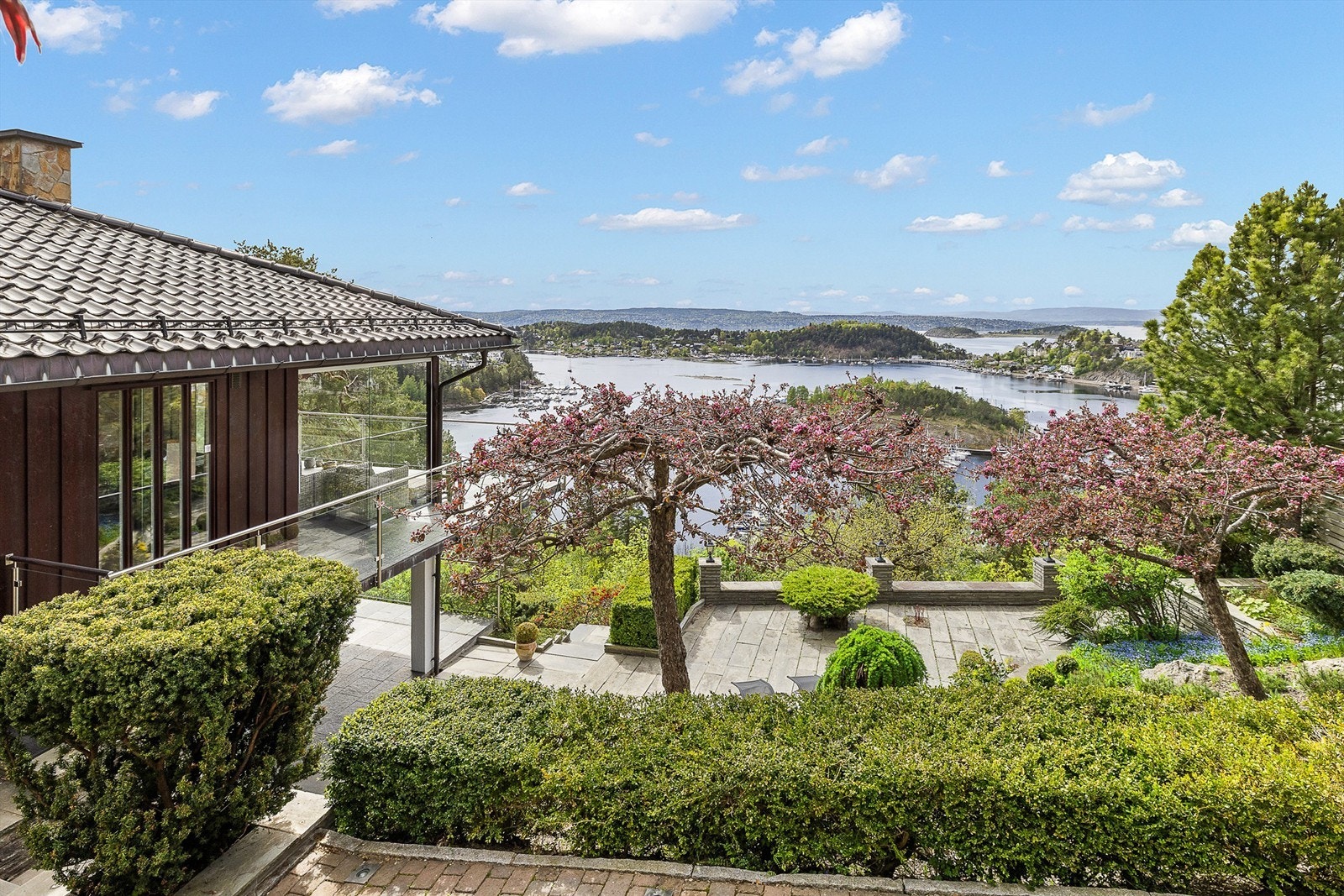 Terrassert tomt som er parkmessig opparbeidet med store skiferbelagte markterrasser, belysning, store bed med prydbusker og et lite flatt plenareal Galleribilde