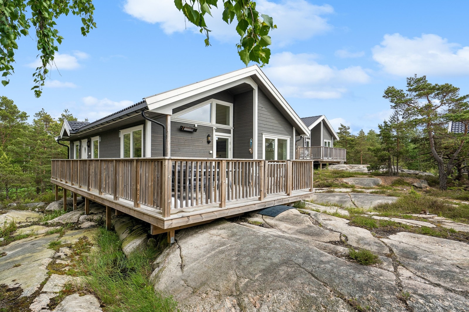 Hytten ligger på en naturtomt med lyng og lave furutrær, noe bjørk. Galleribilde