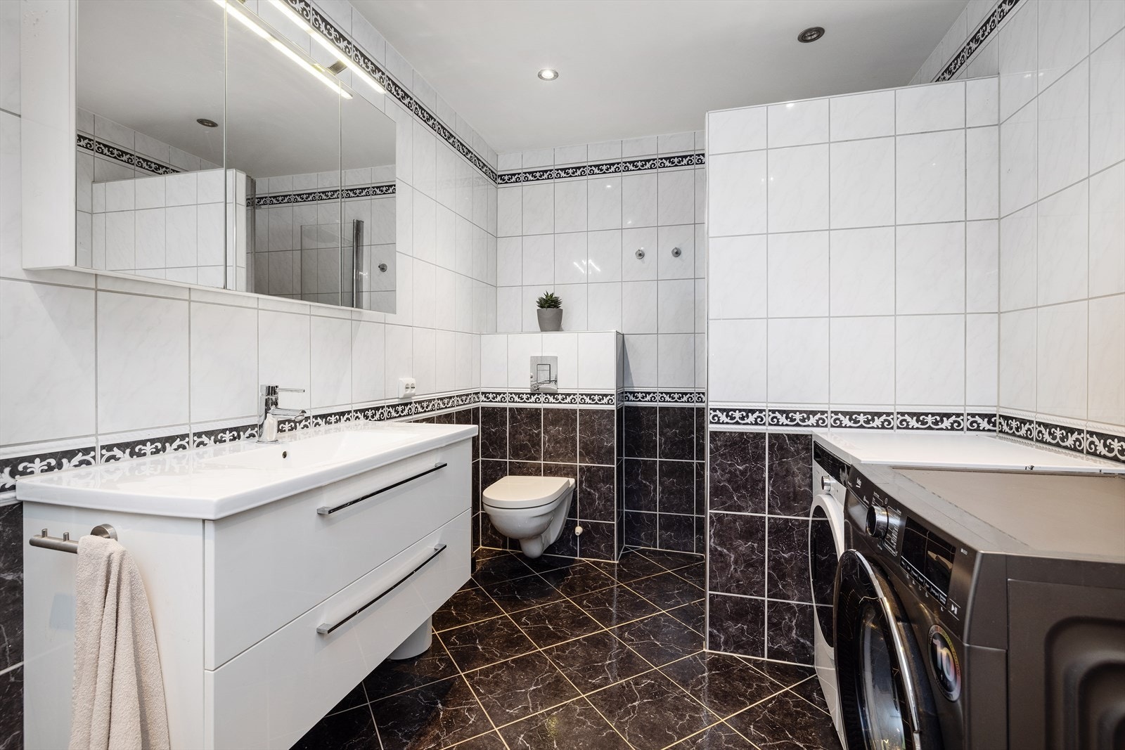 Badet er kombinert vaskerom med vegghengt toalett og opplegg for vaskemaskin. Galleribilde