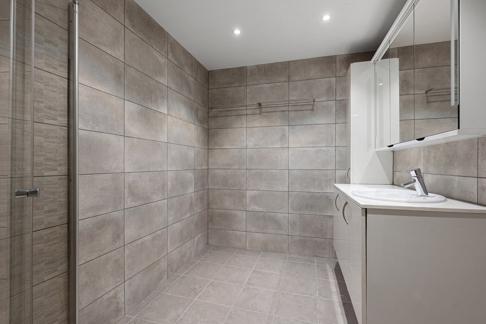 Badet ble oppgradert i 2022 og fremstår moderne med flislagte overflater, downlights i himling, dusjhjørne med glassvegger, servantinnredning og speilskap. Galleribilde