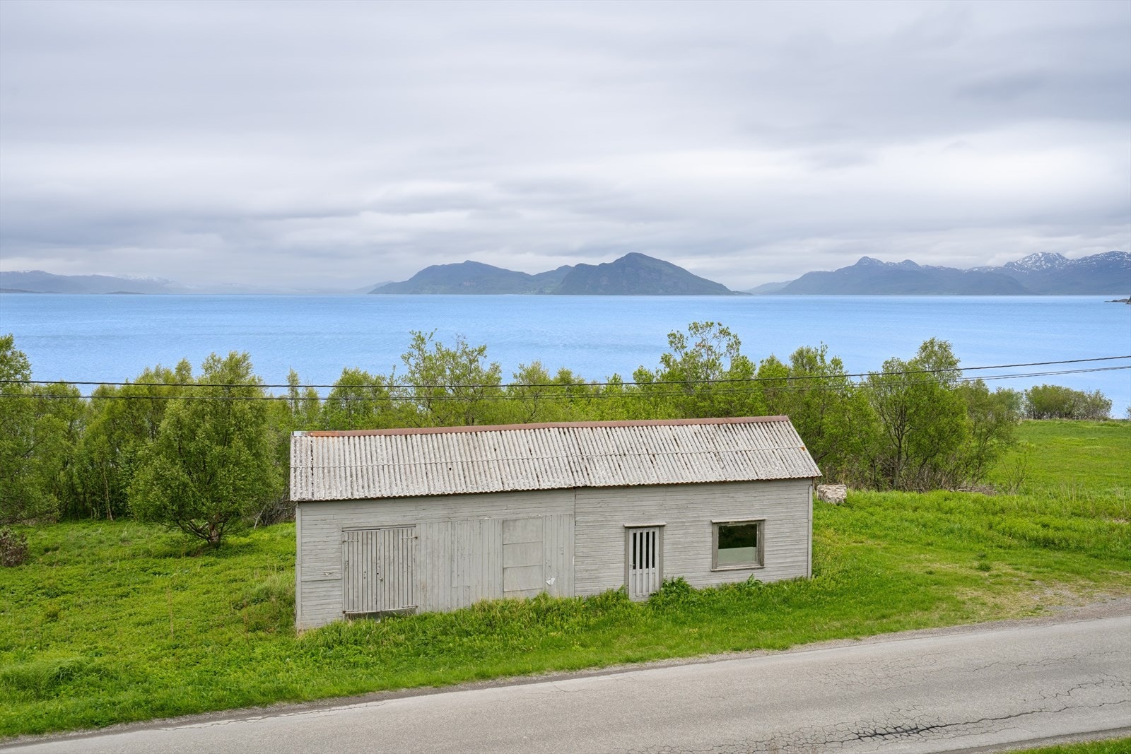 På nedsiden av veien står et eldre bygg som i dag benyttes som lagringsplass og garasje. Galleribilde