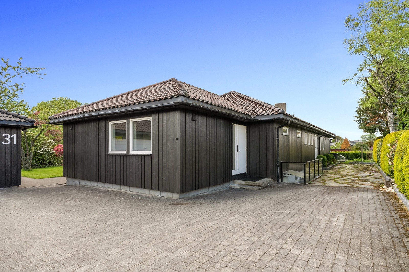 Garasje og steinlagt gårdsrom gir praktiske parkeringsløsninger og kompletterer helhetsinntrykket av en velholdt og innholdsrik familiebolig. Galleribilde