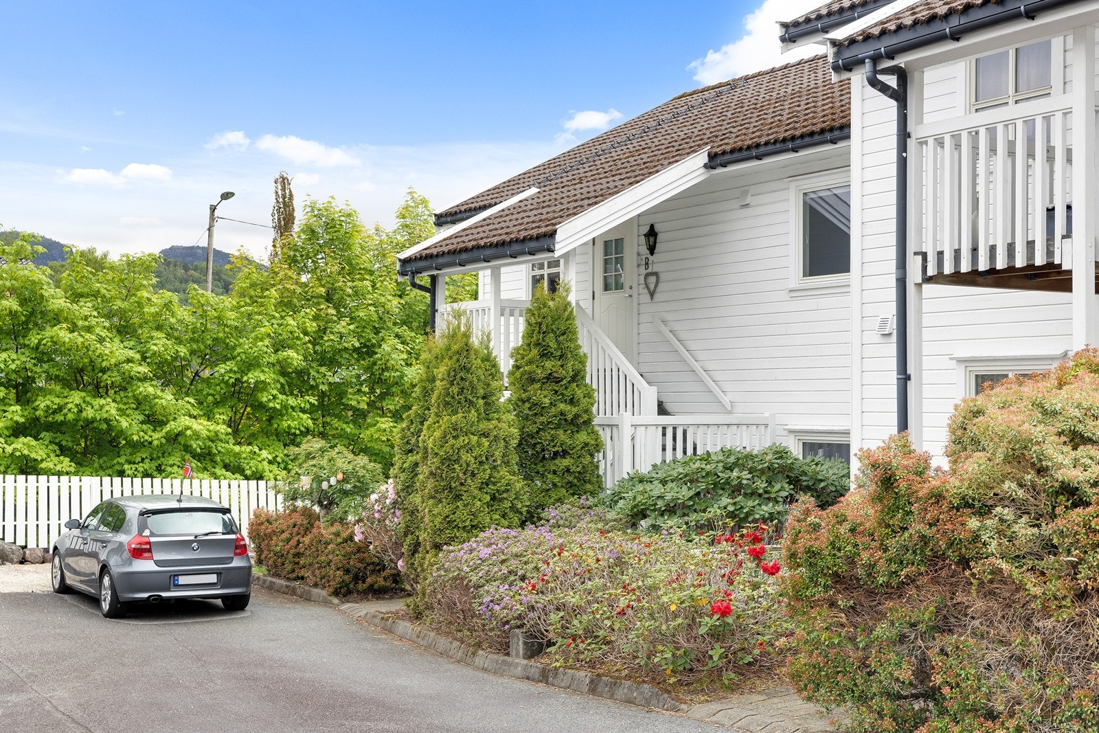 Pent og velholdt boligbygg med hvitmalt trekledning. Enkel adkomst med parkering i garasje like ved boligen, samt pent opparbeidet uteområde rundt bygget. Galleribilde