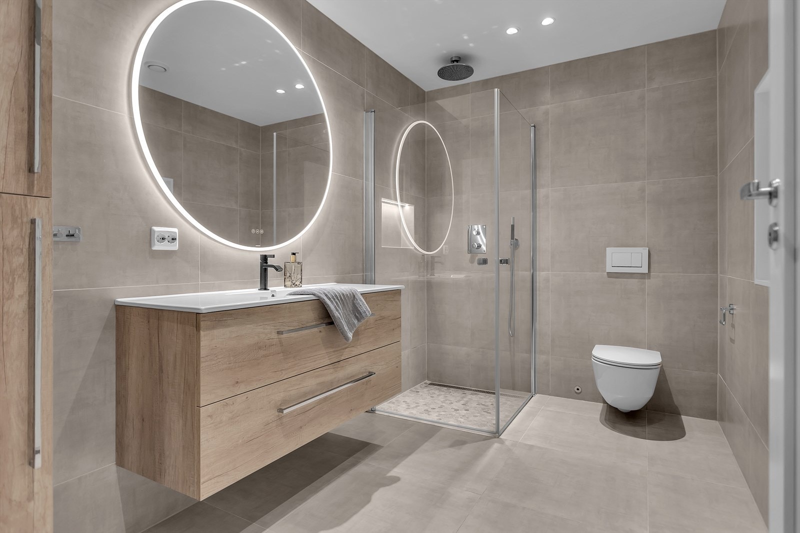 Elegant og helfliset baderom med moderne detaljer. Dusjnisje med plassbesparende glassvegger og regnfallsdusj i taket gir en spa-lignende følelse. Baderommet har også mekanisk avtrekk og varmekabler i gulvet for økt komfort og funksjonalitet. Galleribilde
