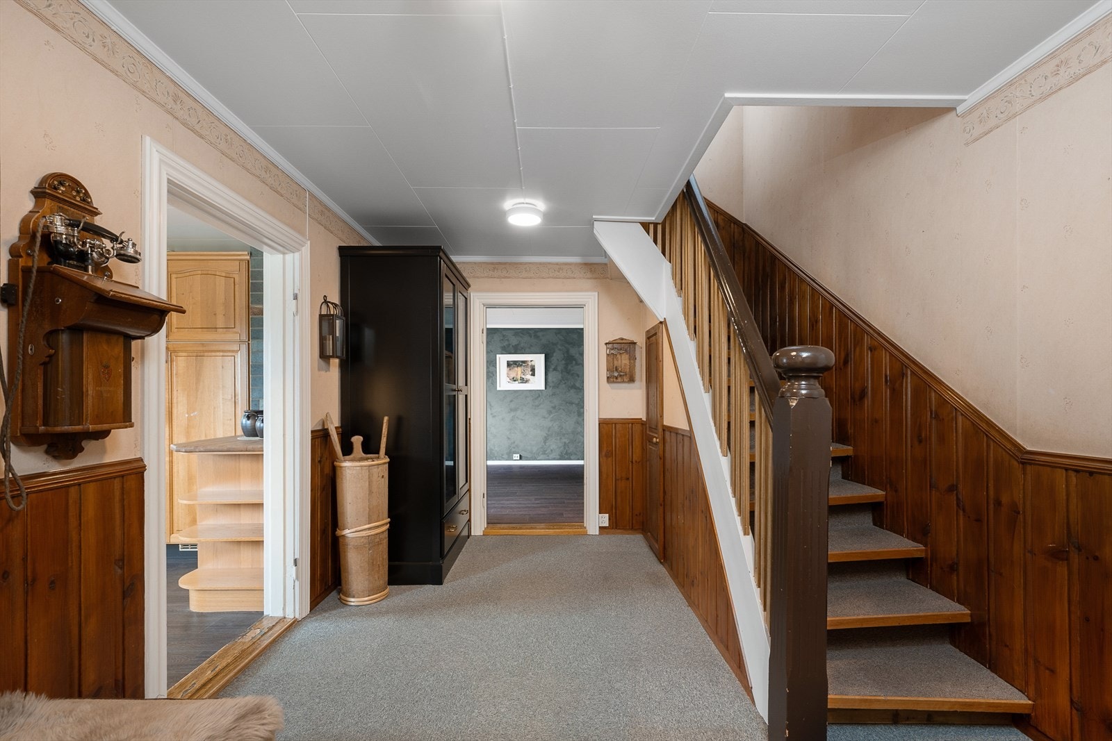 Gang med brystningspanel og trapp i heltre belagt med teppe opp til andre etasje. Galleribilde