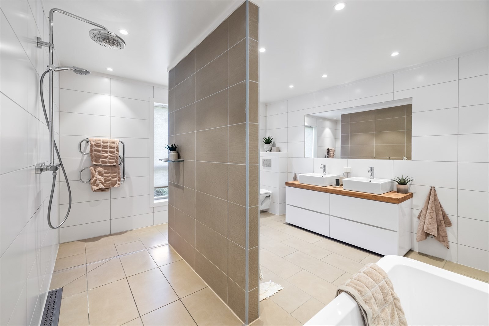Stort bad/wc i mellomplanet. Badet har en romslig utforming og er komplett utstyrt - her får man både badekar og en egen dusjsone med doble regnfallsdusjer. Galleribilde