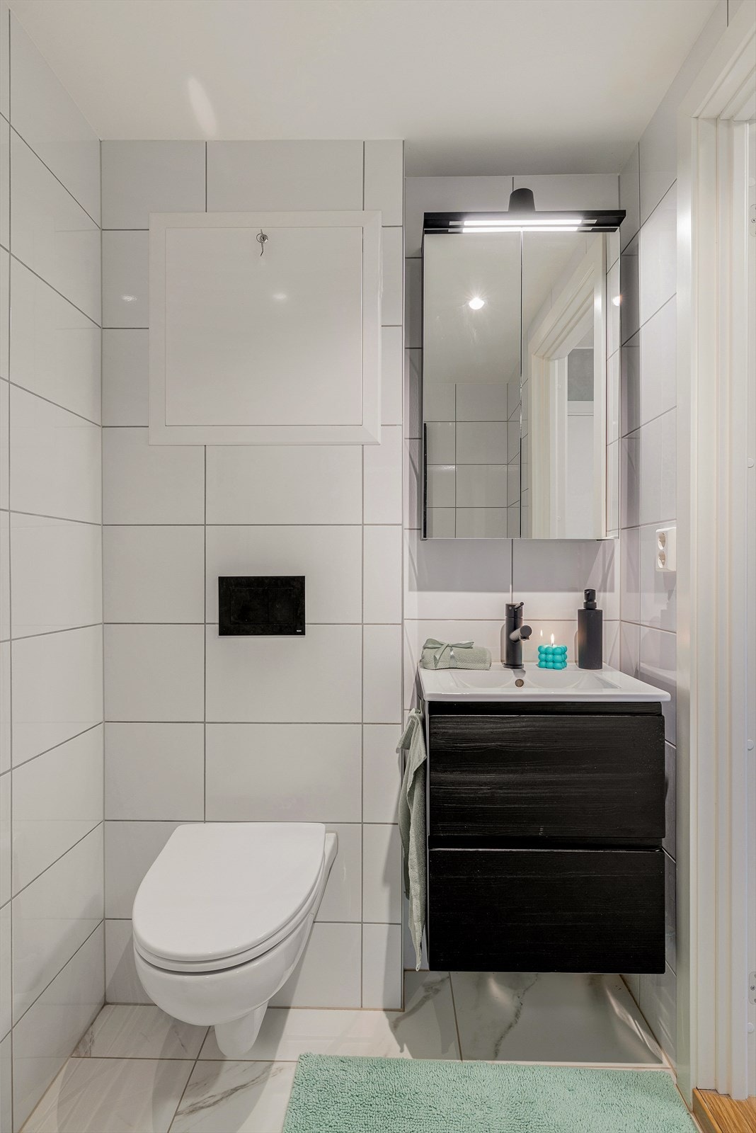 Badet er innredet med veggmontert toalett, nedfelt servant og speilskap med belysning. Galleribilde