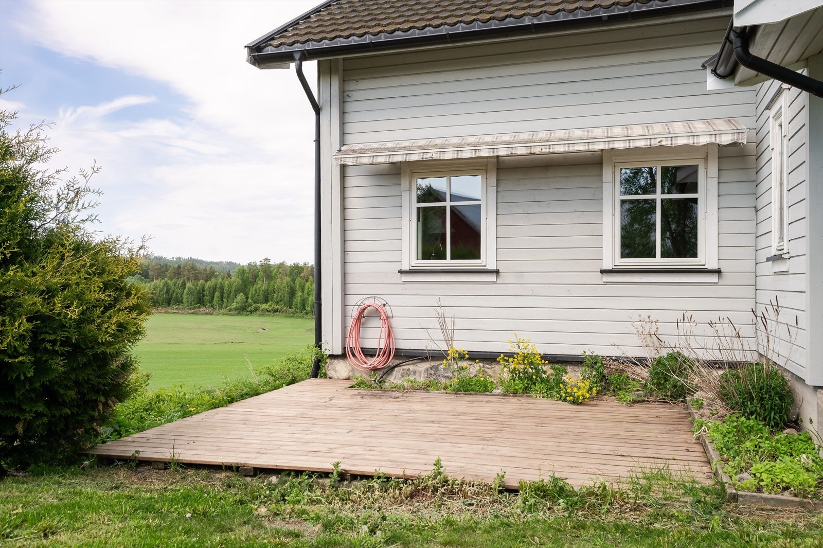 Terrassen har terrassebord på gulv og gode solforhold. Det er koselig blomsterbed ved husveggen og montert markise. Galleribilde