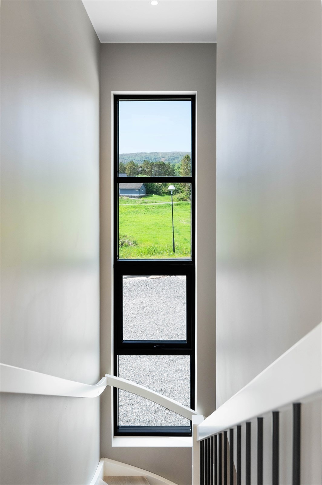 Det høye vinduet opp langs trappeoppgangen gir mye naturlig lysinnslipp og understreker boligens moderne arkitektur. Galleribilde