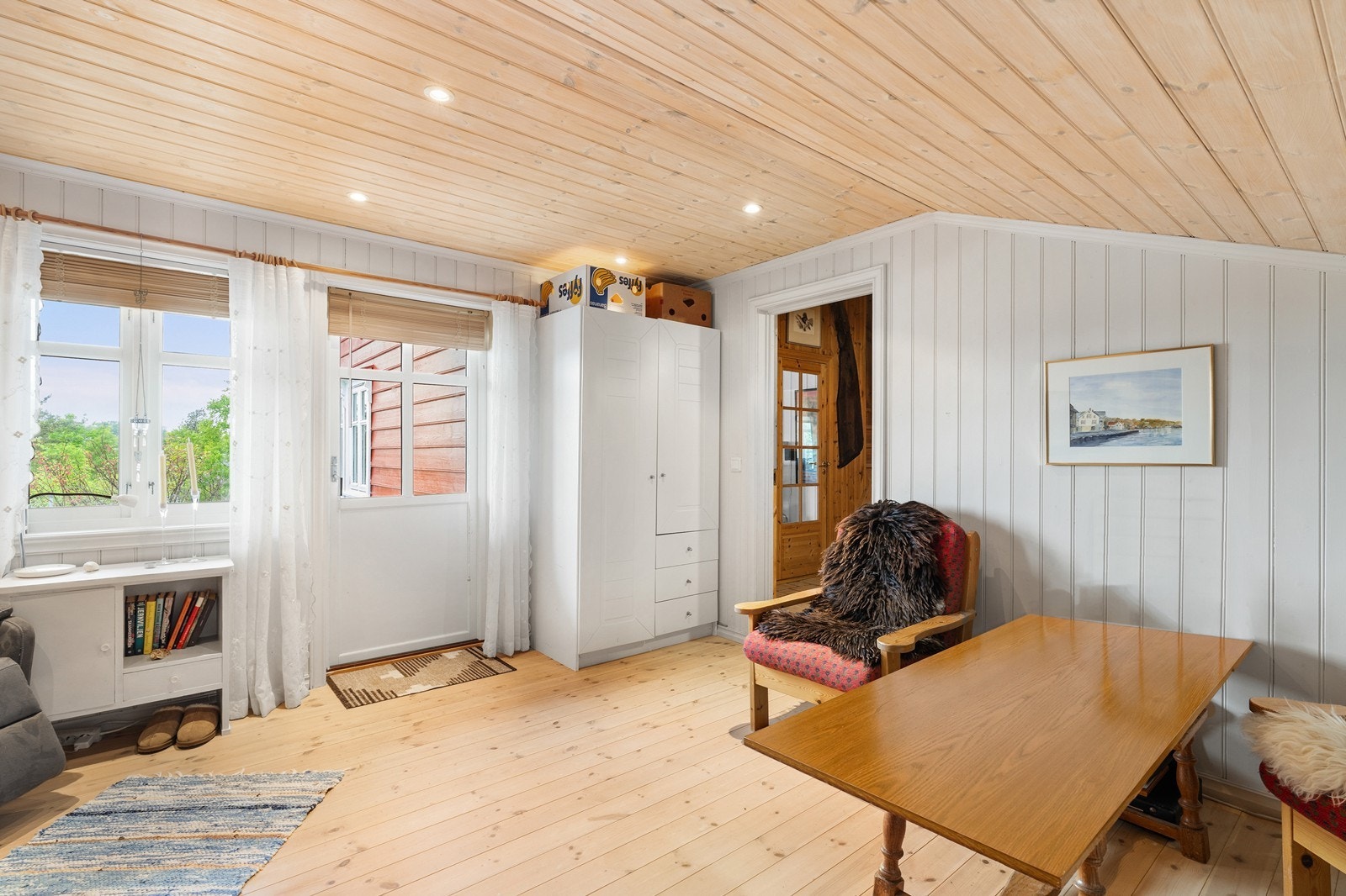 Rommet har panel på gulv og tak samt hvitmalte vegger, noe som gir et lyst og trivelig uttrykk. Fra stuen er det utgang til en hyggelig platting Galleribilde