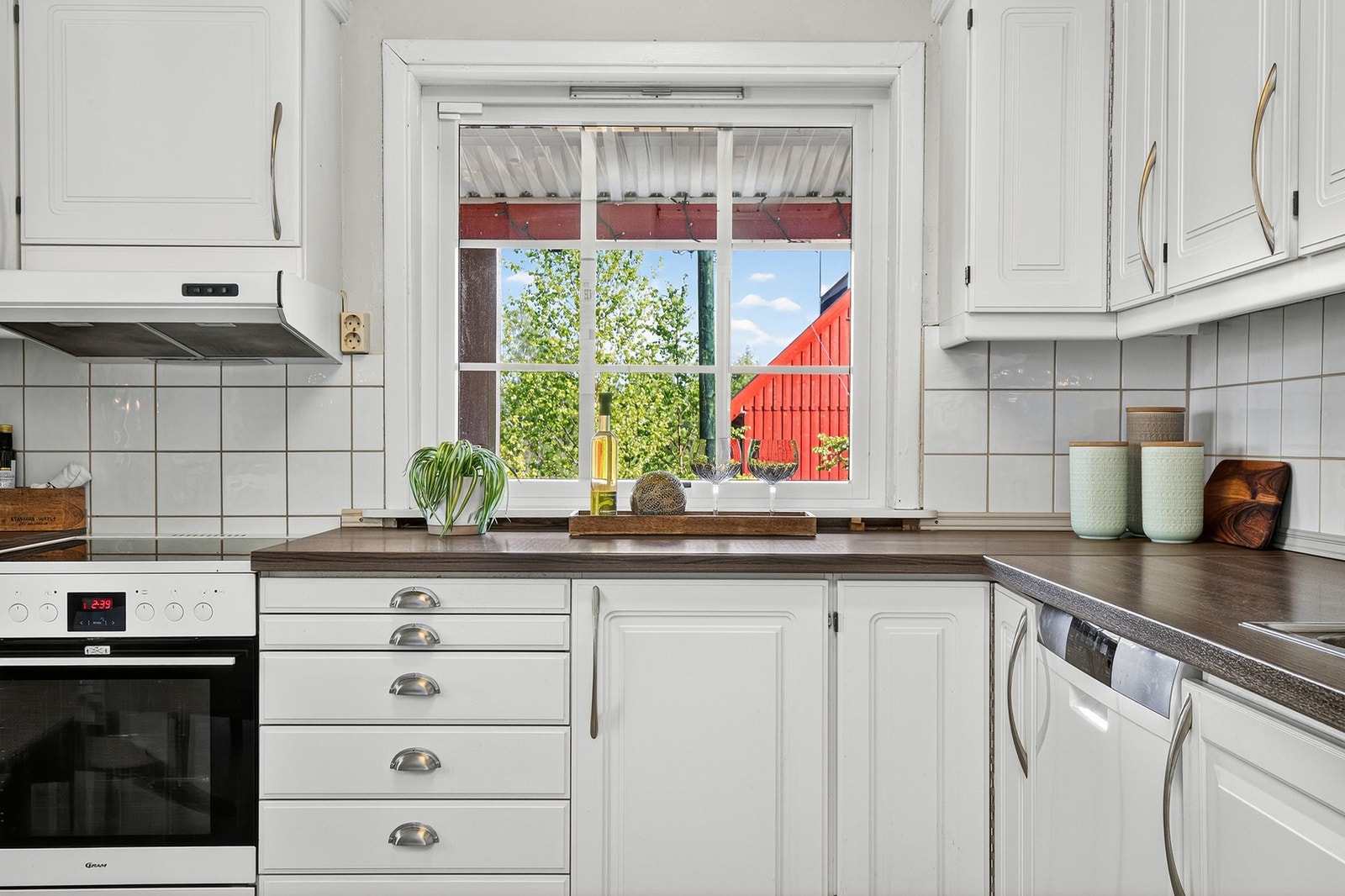 Boligens kjøkken med hvite profilerte fronter, komfyr og plass til vaskemaskin. Galleribilde