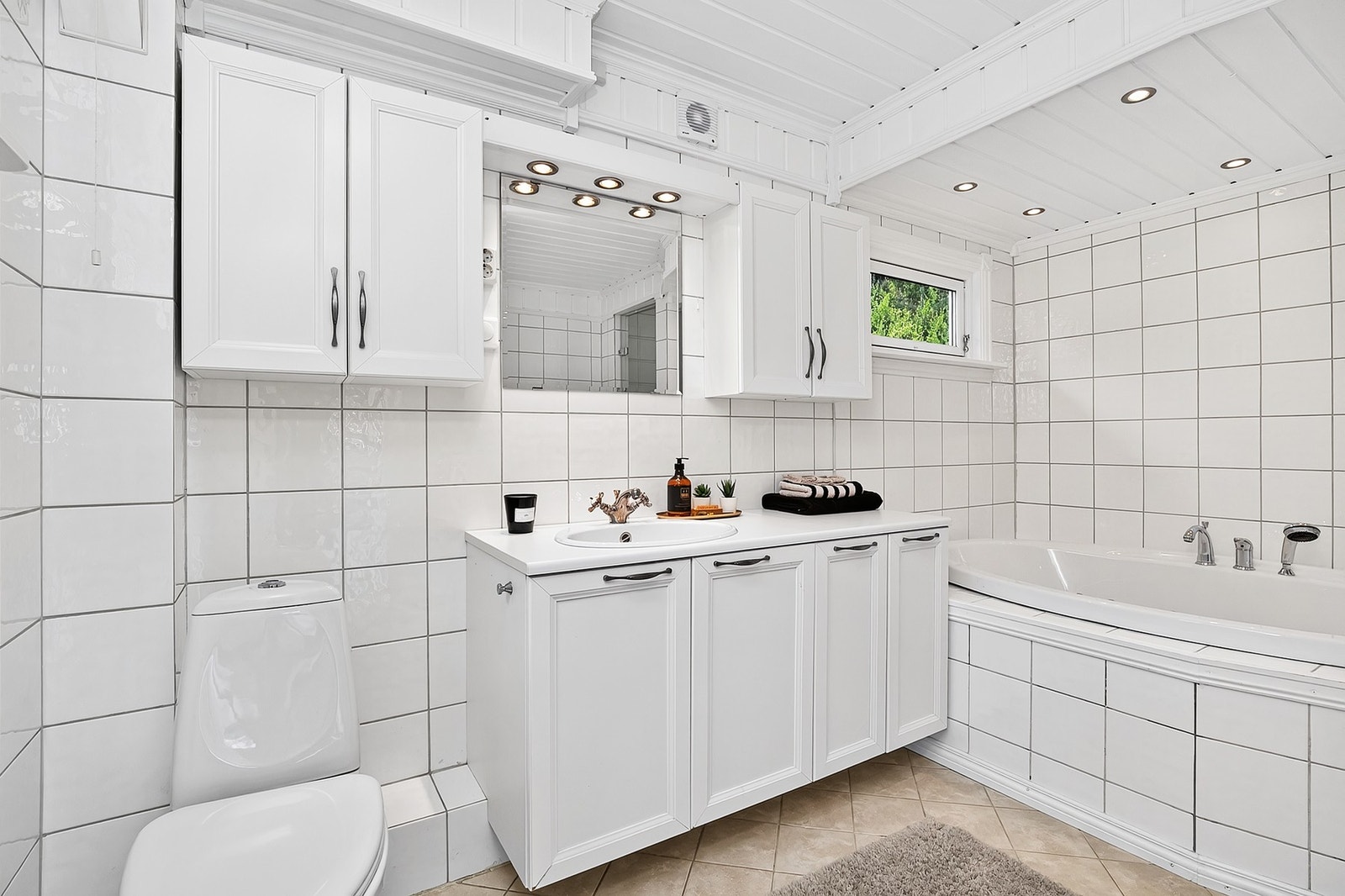 Badet i 1. etasje er utformet med hvite fliser og vegghengt interiør. Badekar, gulvstående toalett og spotter i tak. Galleribilde