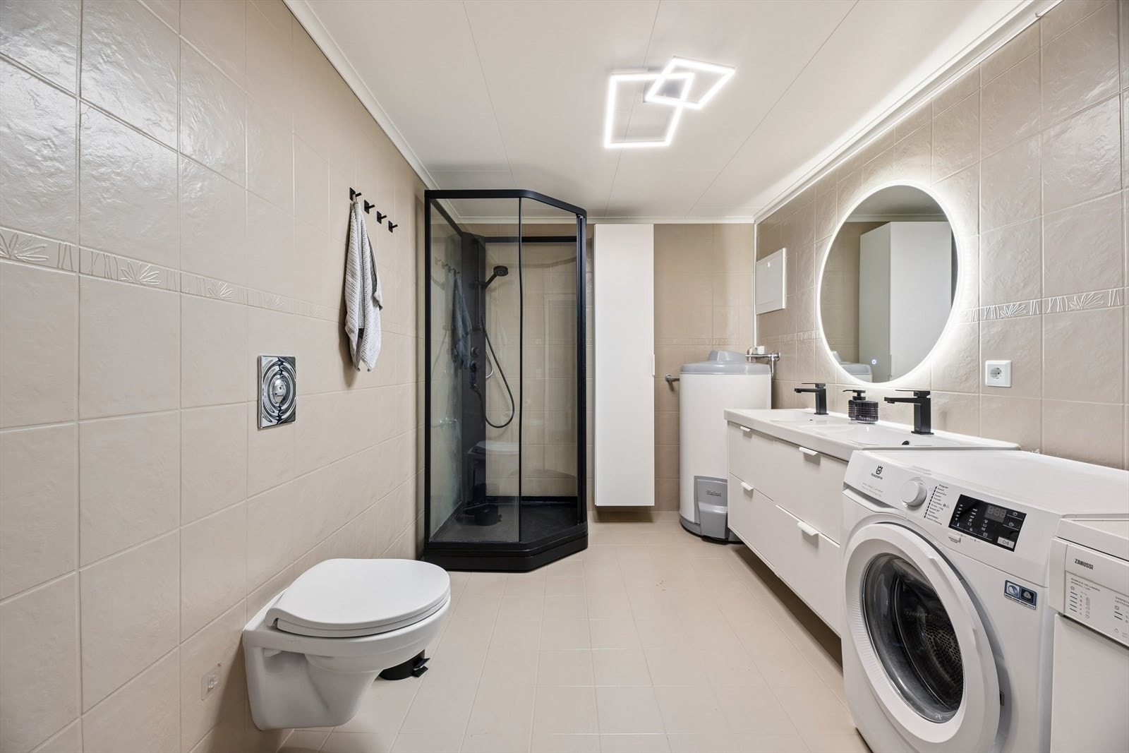 Badet er utstyrt med vegghengt toalett, dusjkabinett, dobbelt skap med nedfelt servant, samt varmtvannsbereder og opplegg for vaskemaskin. Galleribilde