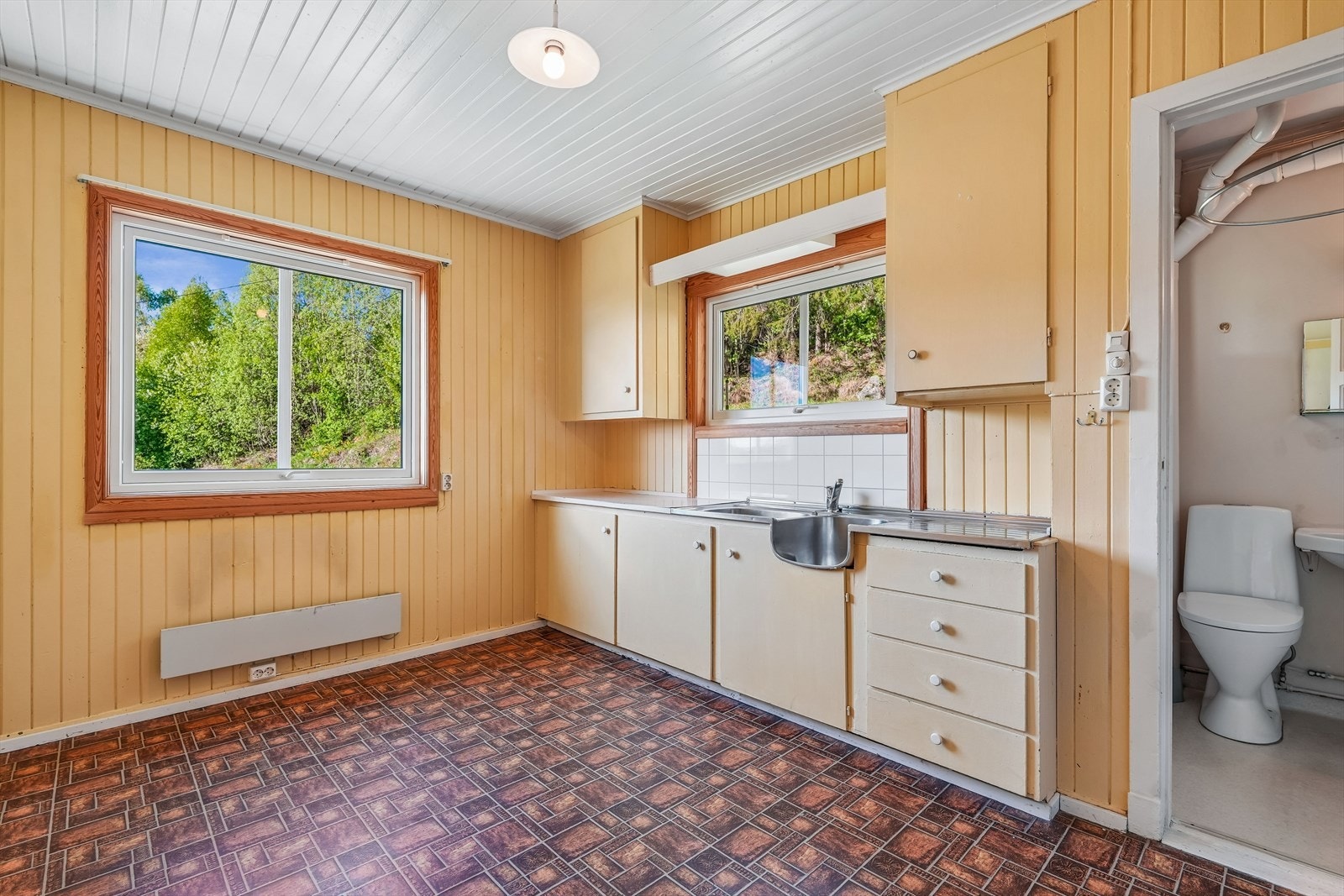 Kjøkkenet har en eldre innredning med malte fronter, over- og underskap, malt trebenkeplate og oppvaskkum i stål. Det er ikke etablert ordinære kokemuligheter på kjøkkenet. Galleribilde