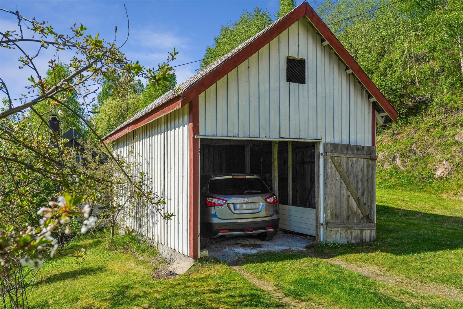 På eiendommen står også en enkel garasje-/uthusbygning. Bygningen har tidligere fungert som garasje, men skader på porten gjør at den i dag fremstår mer som en åpen carport. Galleribilde