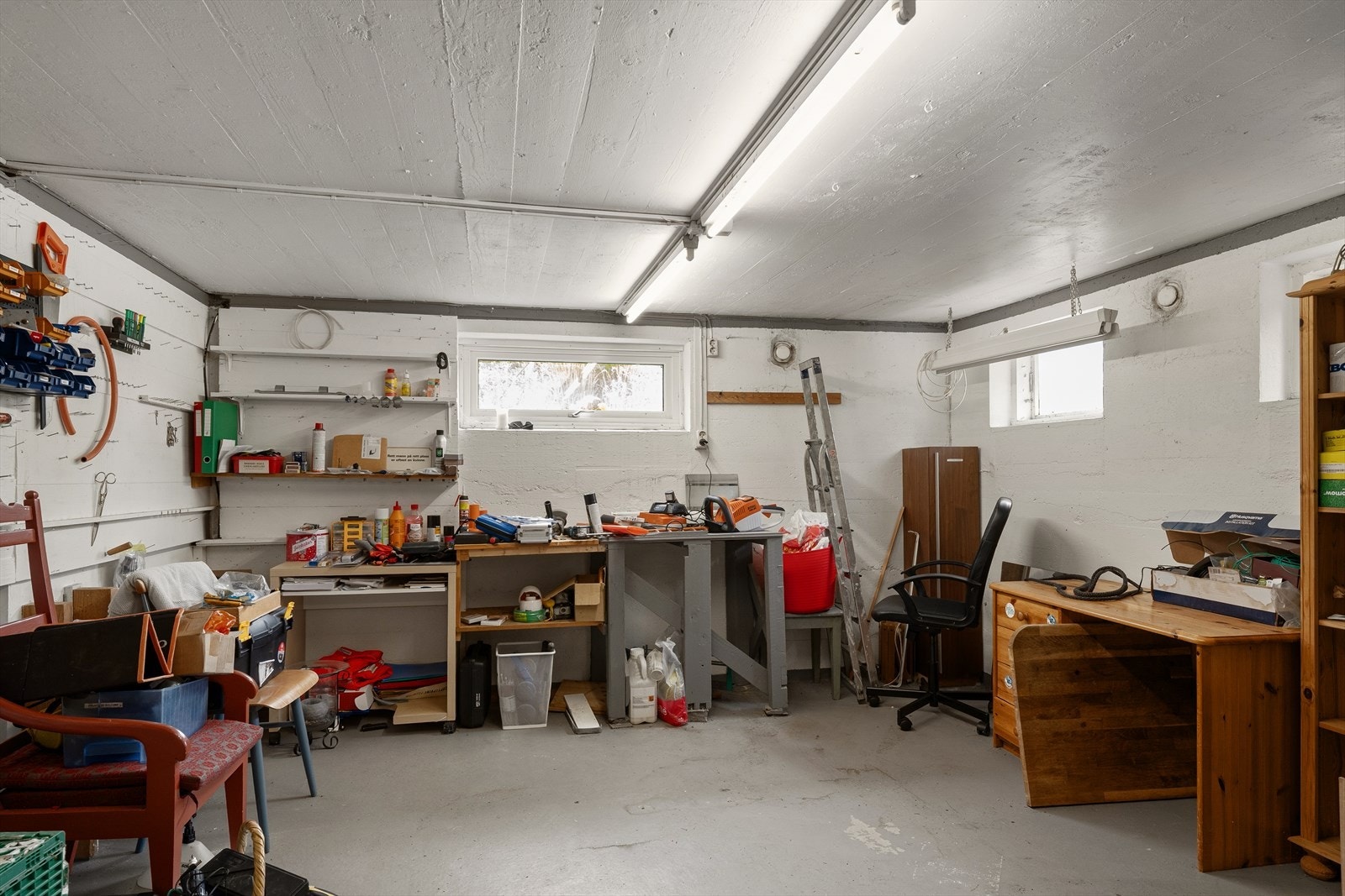 Praktisk kjeller med betonggulv, innredet som verksted og med flere boder for lagring. Galleribilde