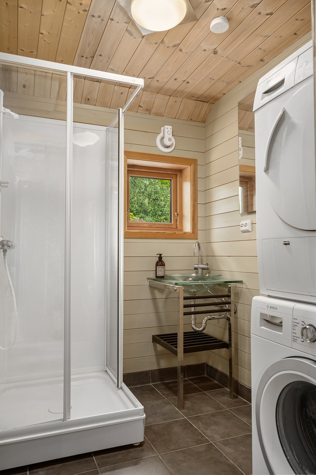 Badet i hoveddelen har flislagt gulv, panel på veggene, dusjkabinett og opplegg for vaskemaskin. Galleribilde