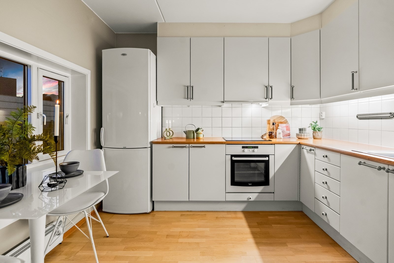 Ved vinduet er det rom for en hyggelig, liten spiseplass. Innredningen er oppført i en smart u-form med god skapplass, hvite, glatte fronter, dobbel oppvaskkum og benkeplate av laminat. Galleribilde