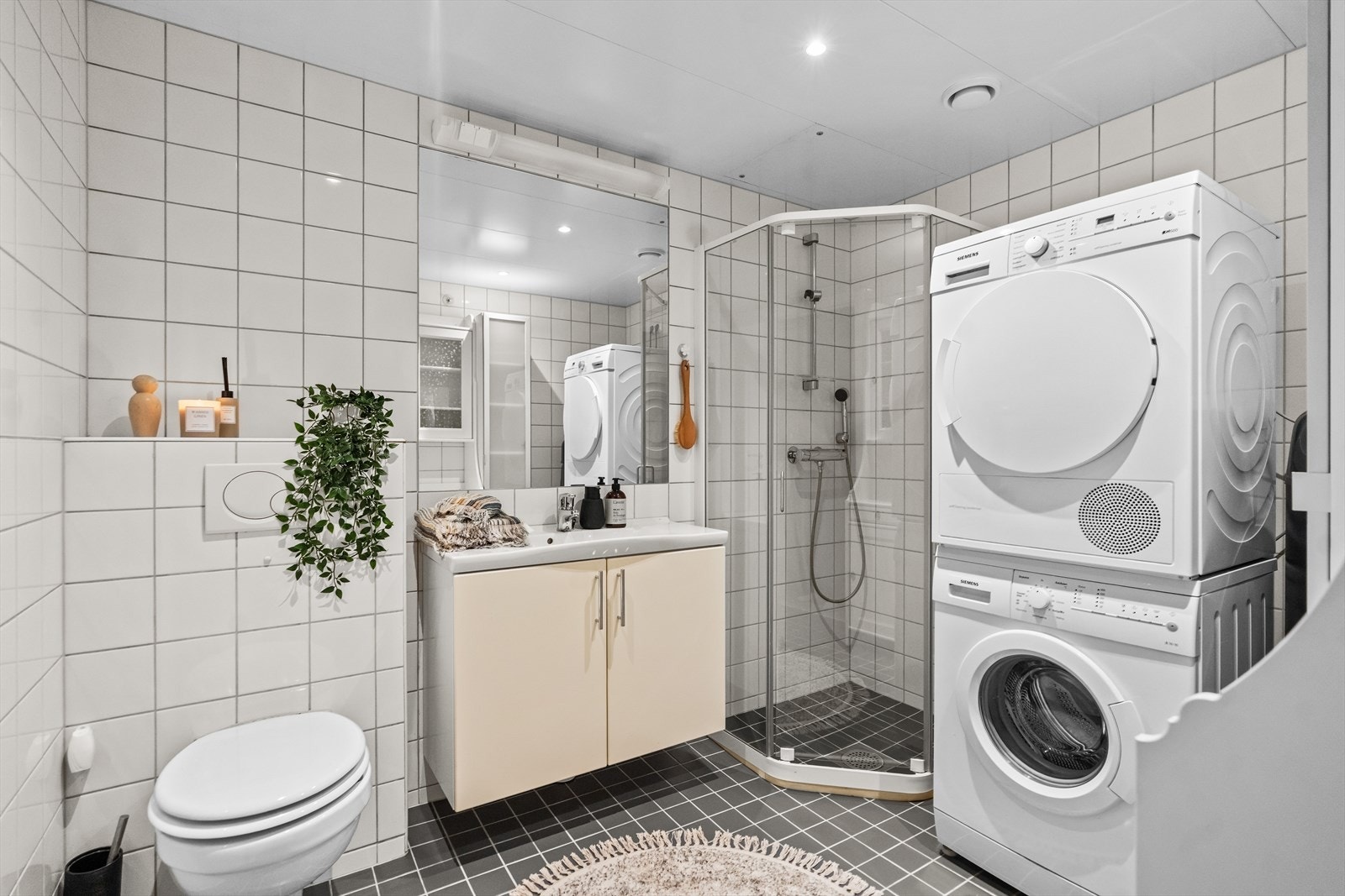Dagene får en fin start på badet, innredet med hvite veggfliser og grå mosaikkfliser på gulvet. Opplegg for vaskemaskin er etablert, og badet har varmekabler, downlights og vegghengt toalett. Galleribilde