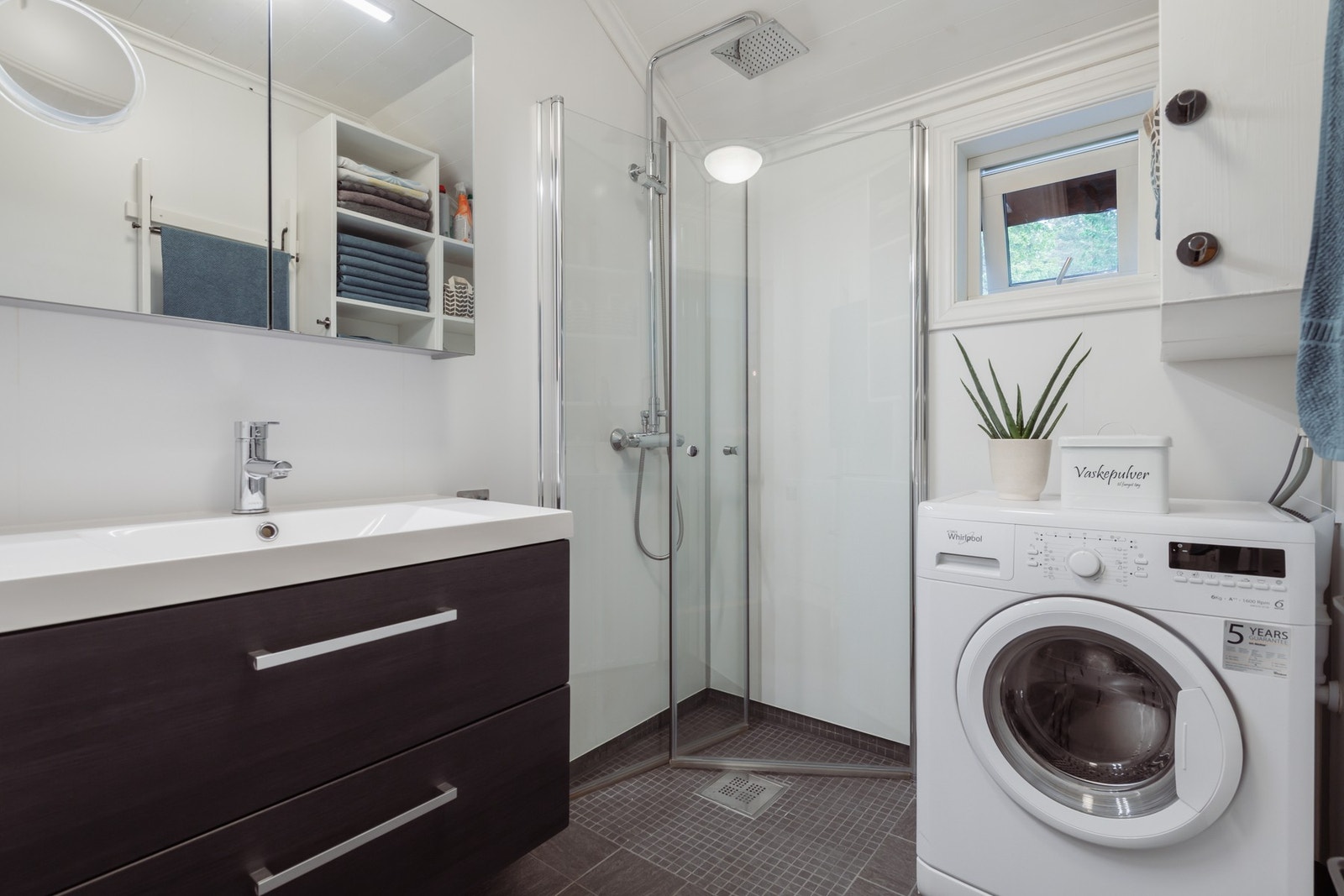 Badet har mørke gulvfliser og hvite våtromsplater i flismønster. Varme er lagt i gulvet, og et dusjhjørne er utstyrt med regnfallsdusj og innfellbare glassdører. I tillegg er det separat toalettrom. Galleribilde