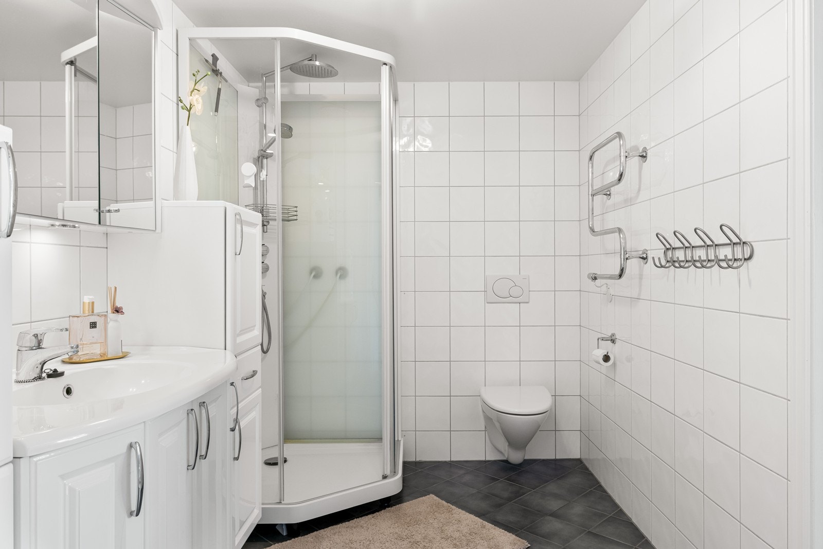 Badet er utstyrt med vegghengt toalett, dusjkabinett og en praktisk håndkletørker. Galleribilde