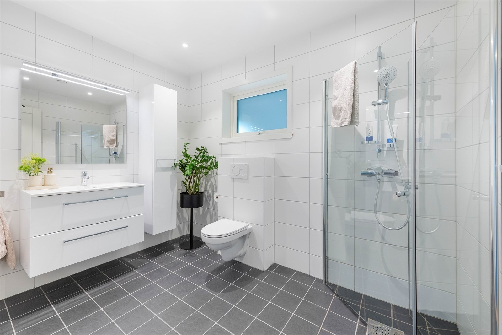 Badet i første etasje er helfliset og betjener soverommene i etasjen. Det er lyse fliser på veggene og mørkere grå fliser på gulv. Galleribilde